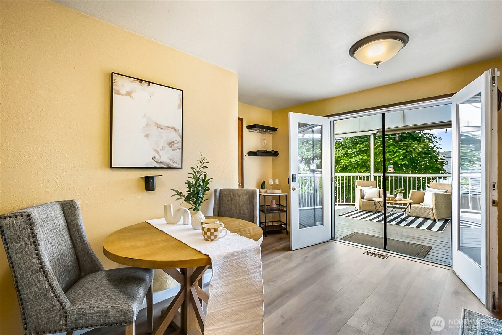 Dining area with a round wooden table and gray chairs opening onto a furnished deck.