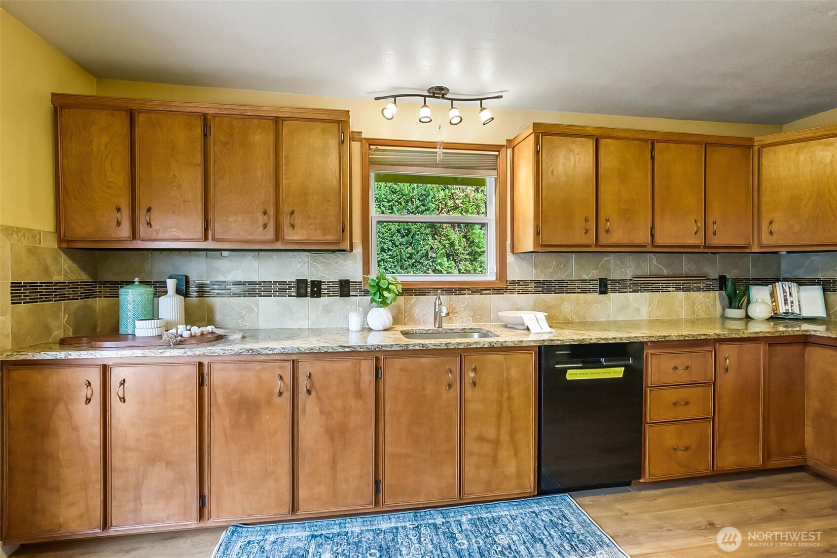 Kitchen with honey-colored wood cabinets, stone counters, tiled backsplash, and a window above the sink.