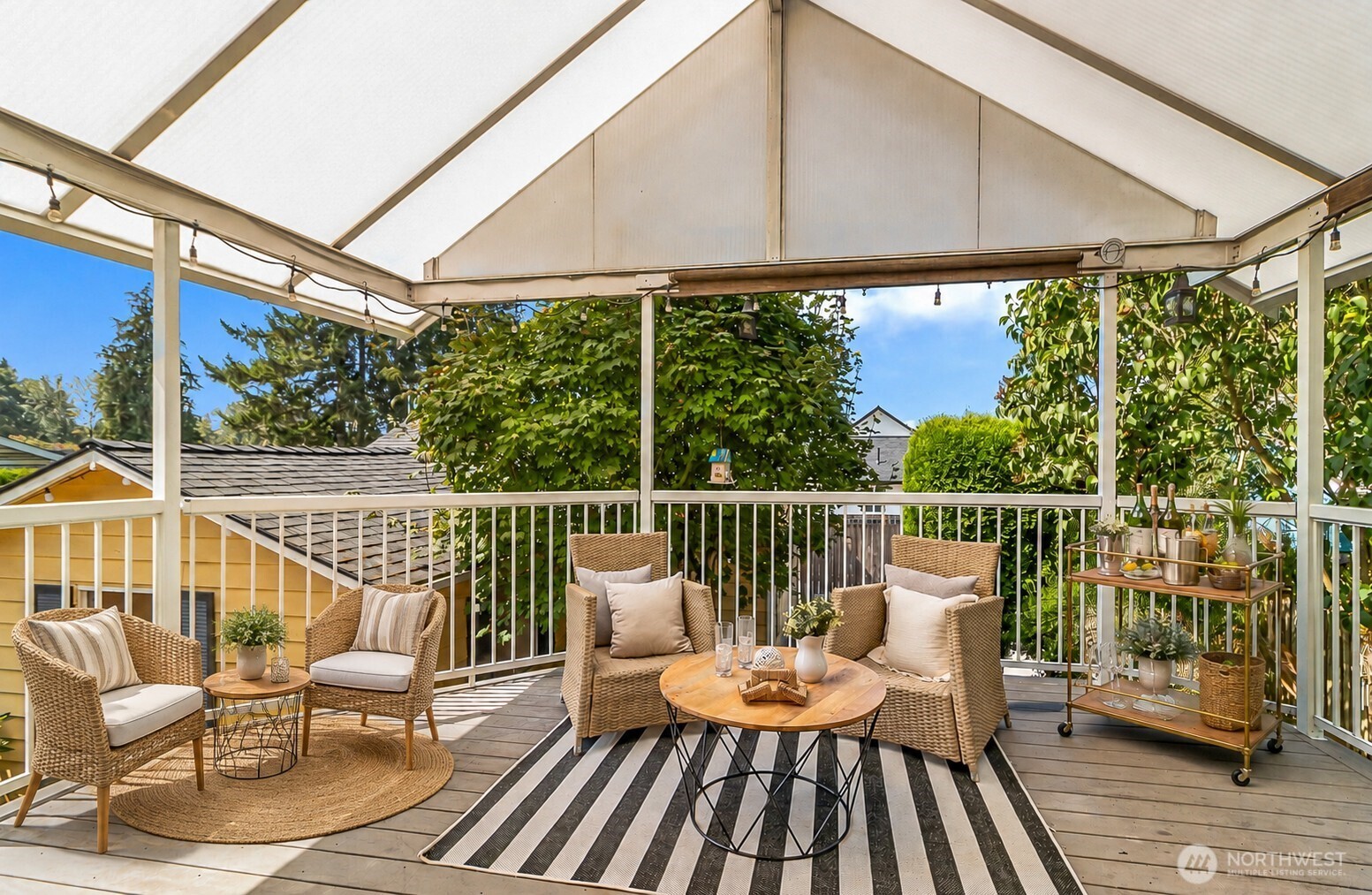 Covered deck with wicker seating, a round table, and leafy trees beyond the railing.