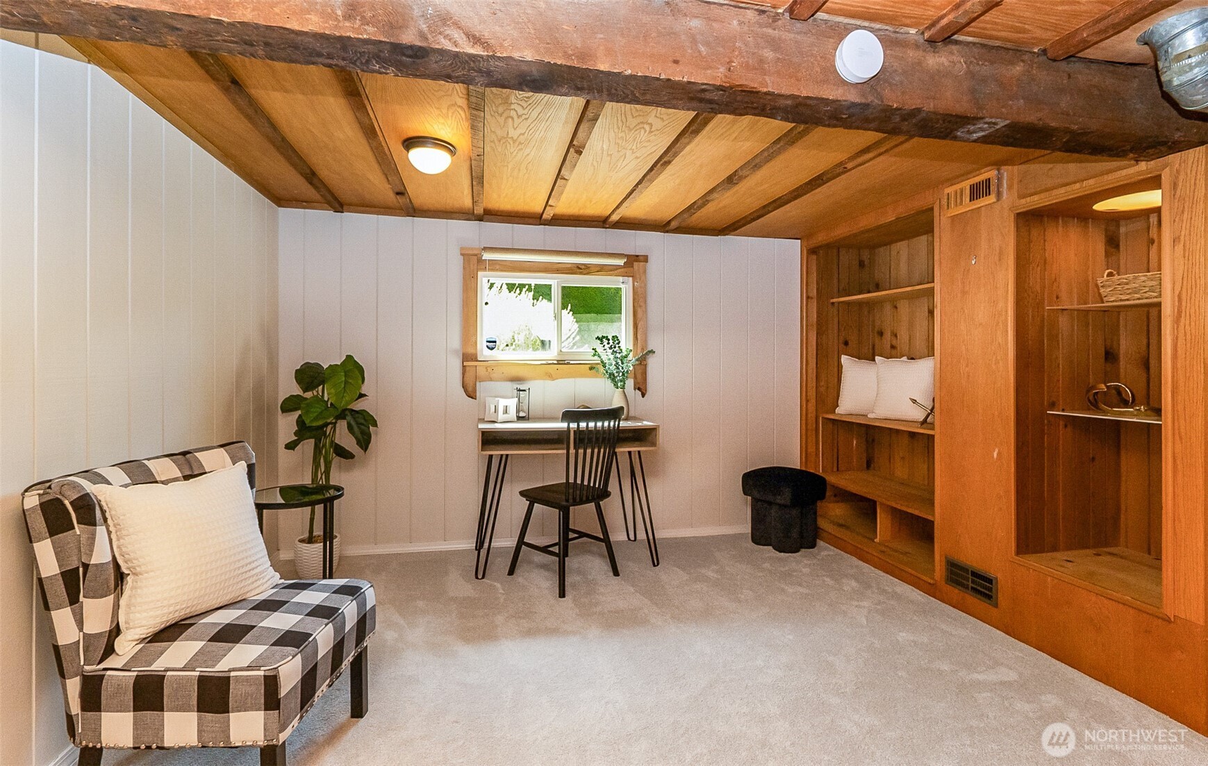 Furnished room with exposed wood beams, built-in shelving, a desk, and a checkered chair.