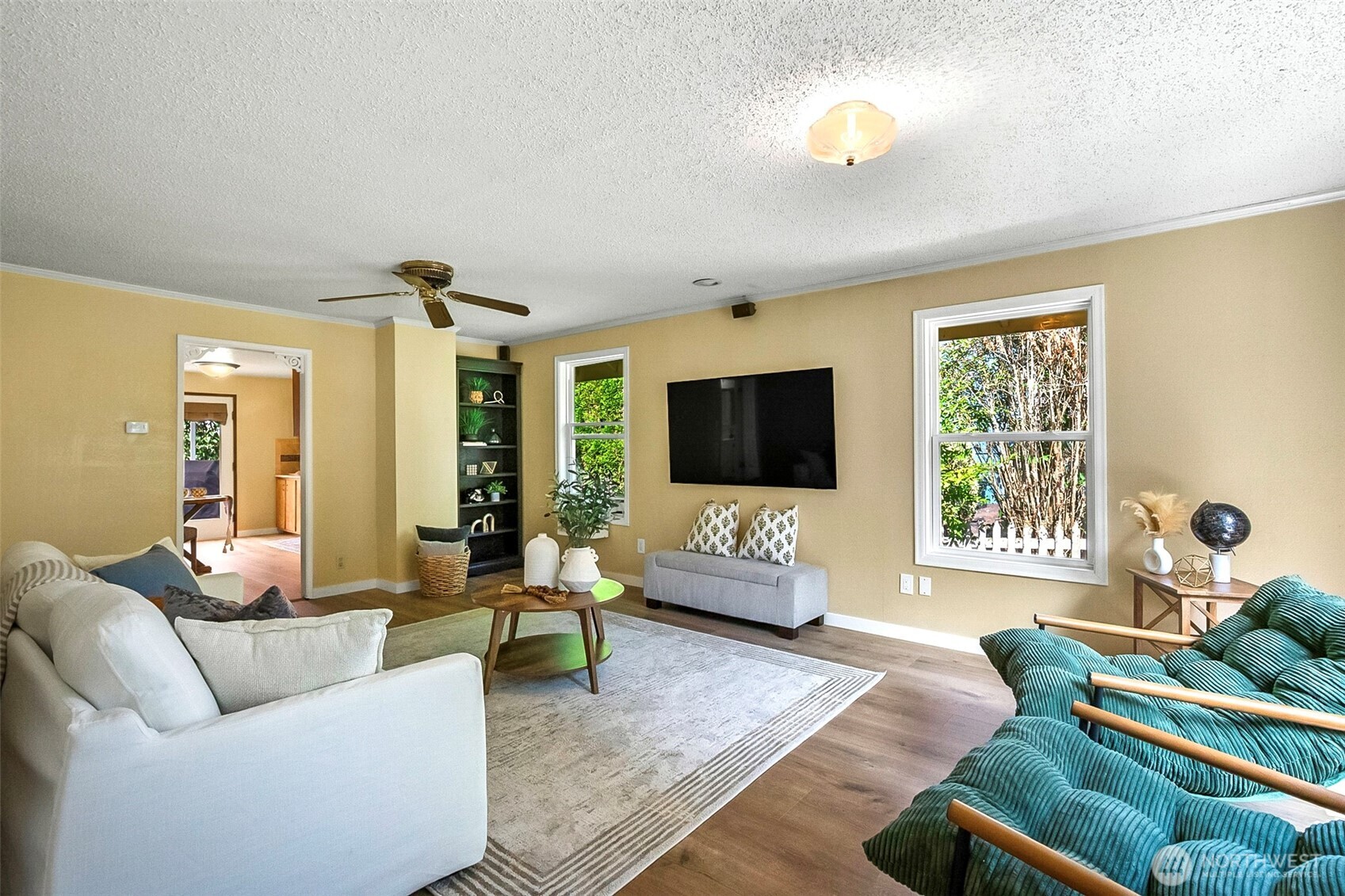 Staged living room with a white sofa, teal armchairs, and wall-mounted television.