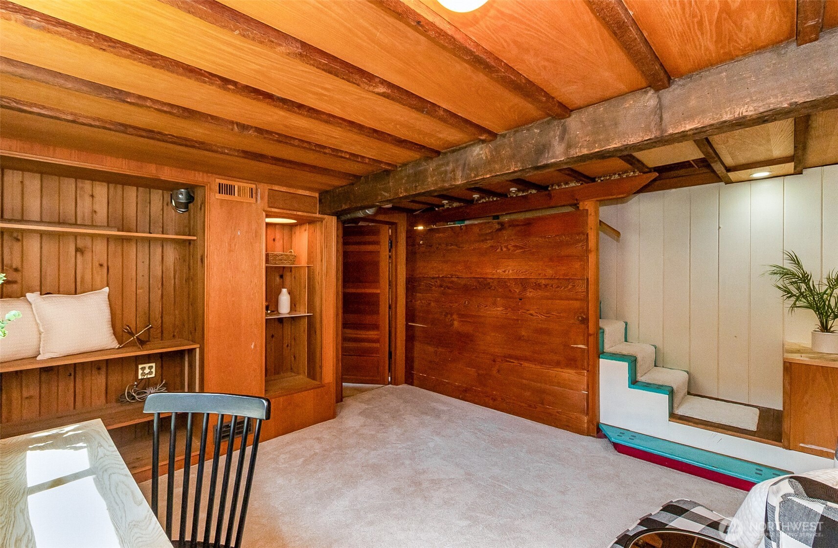 Furnished wood-paneled room with exposed beams, built-in shelving, and stairs.