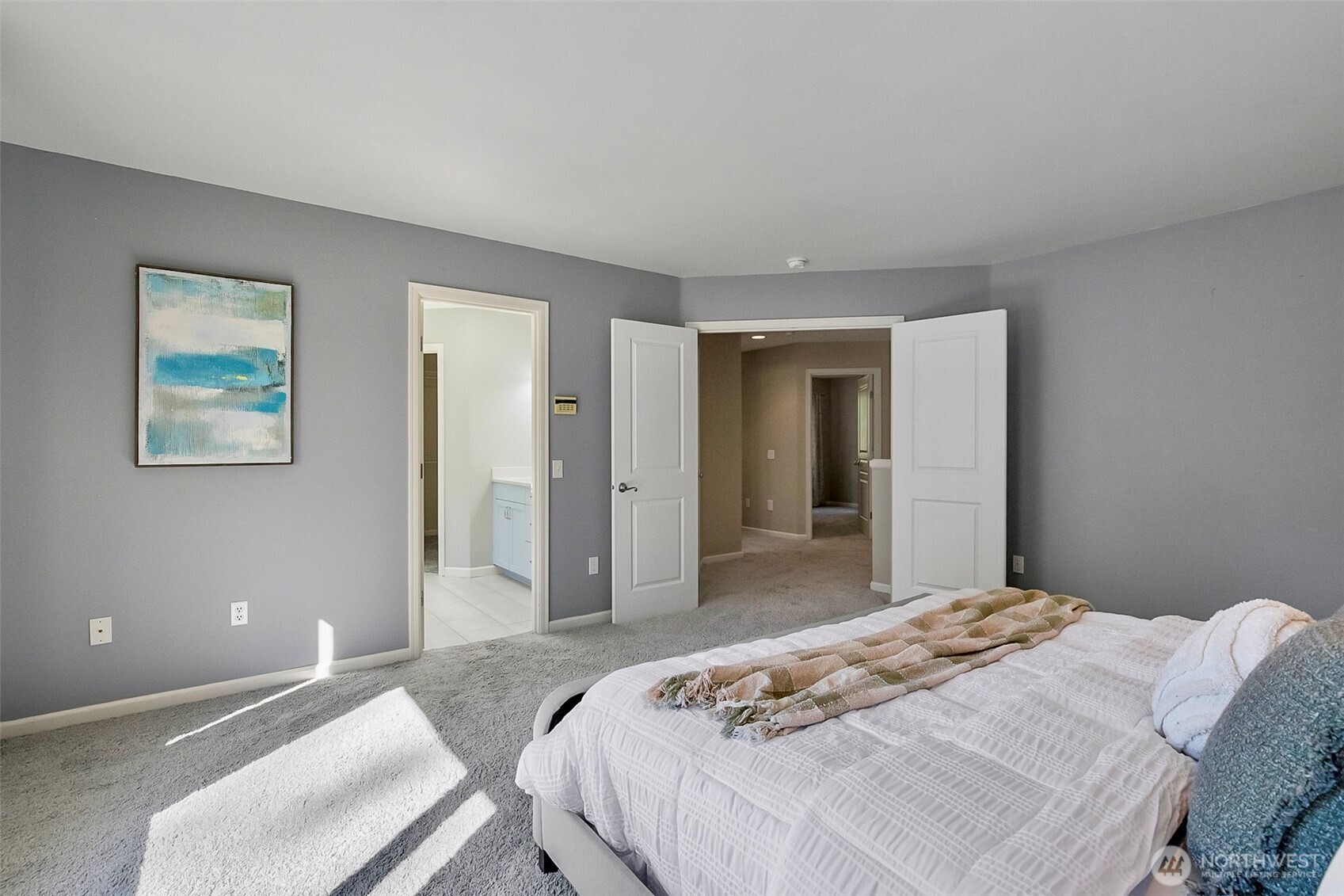 Furnished bedroom with a white bed, gray carpet, and open doors to a hallway and bathroom.