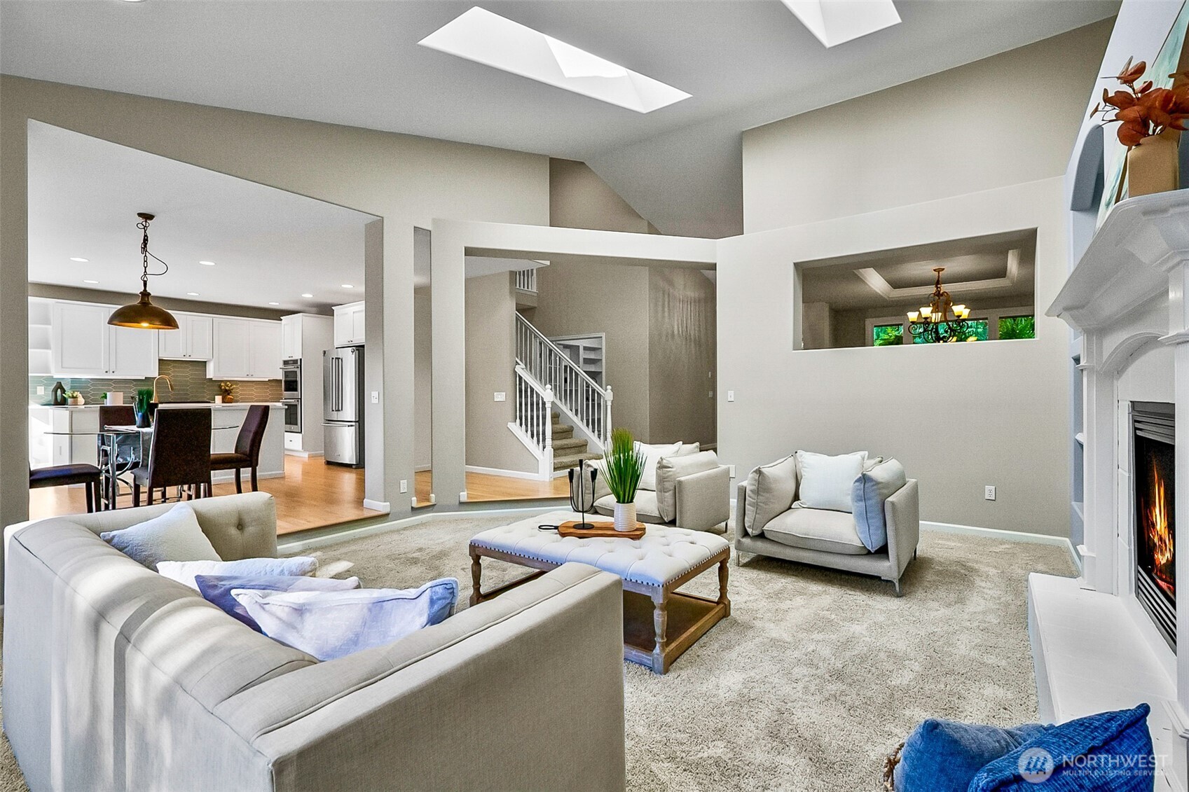 Living room with a white fireplace, light-colored seating, and an open kitchen beyond.