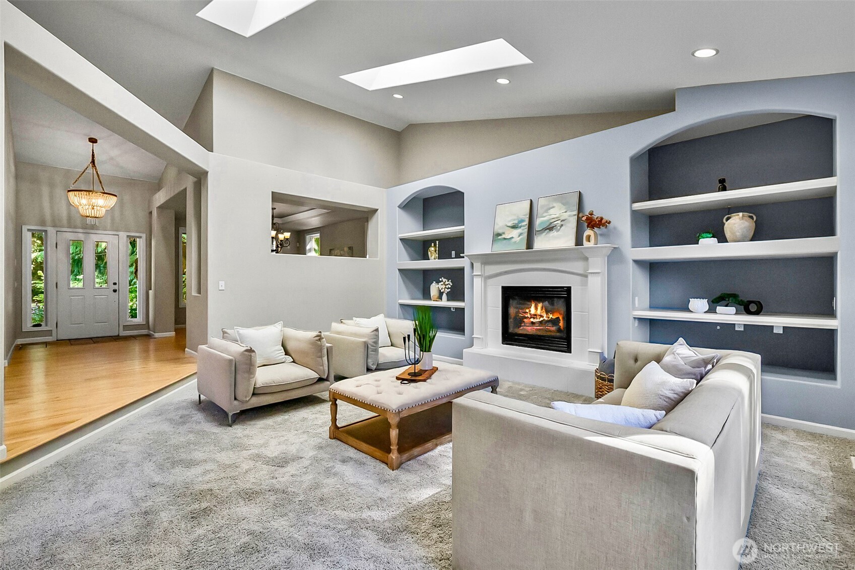 Staged living room with a lit fireplace, built-in shelving, and skylights.