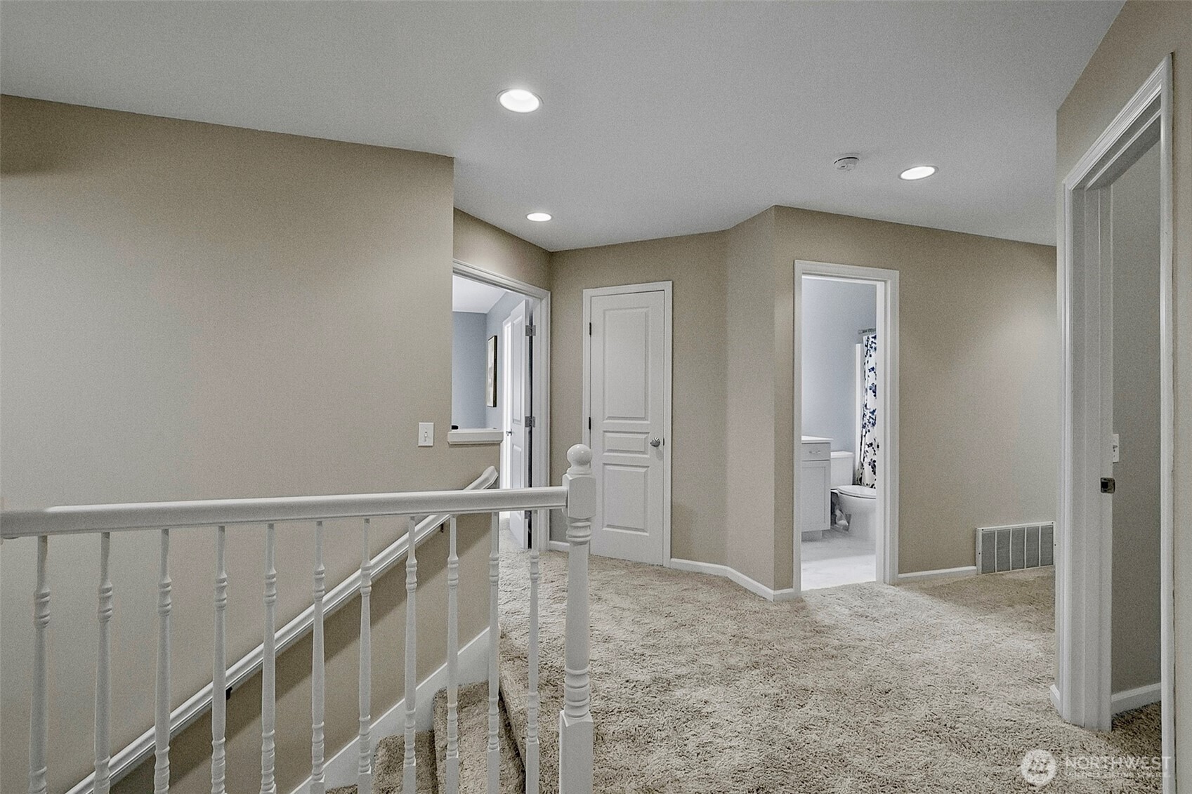 Upstairs hallway with beige carpet, white railing, and an open bathroom doorway.
