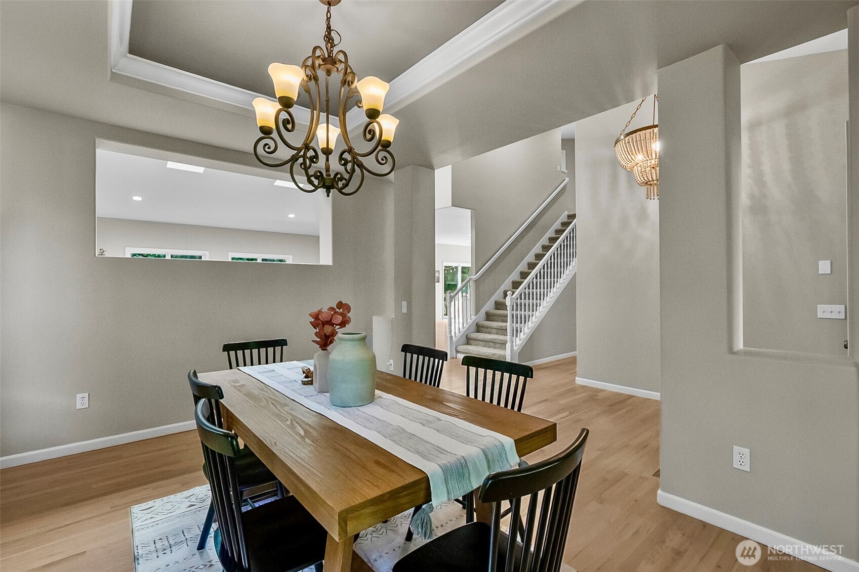 Dining room with a long wooden table, chandelier, and staircase in the background.