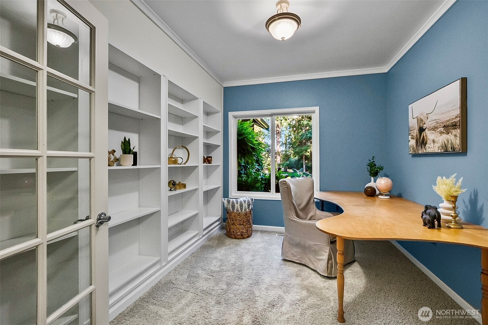 Home office with blue walls, built-in bookshelves, a wood desk, and a garden view.