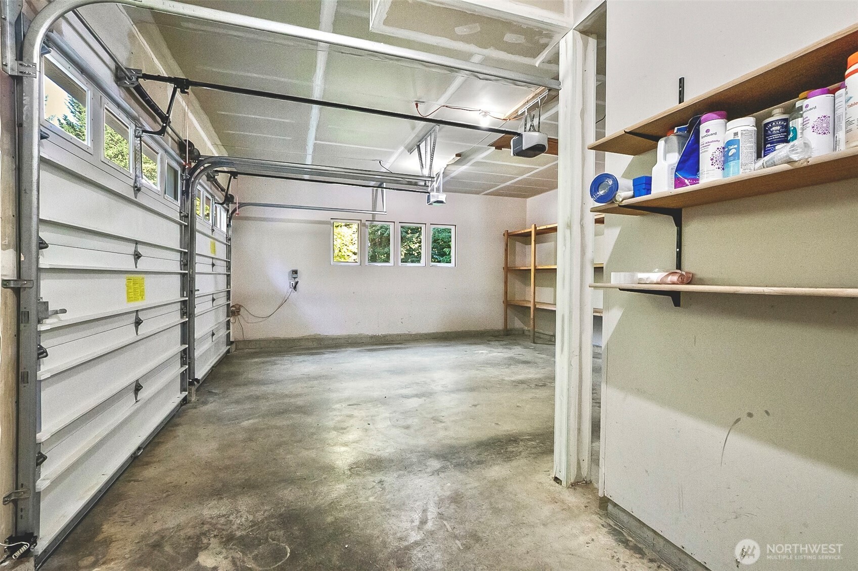 Garage with two overhead doors, a concrete floor, and storage shelves along the right wall.