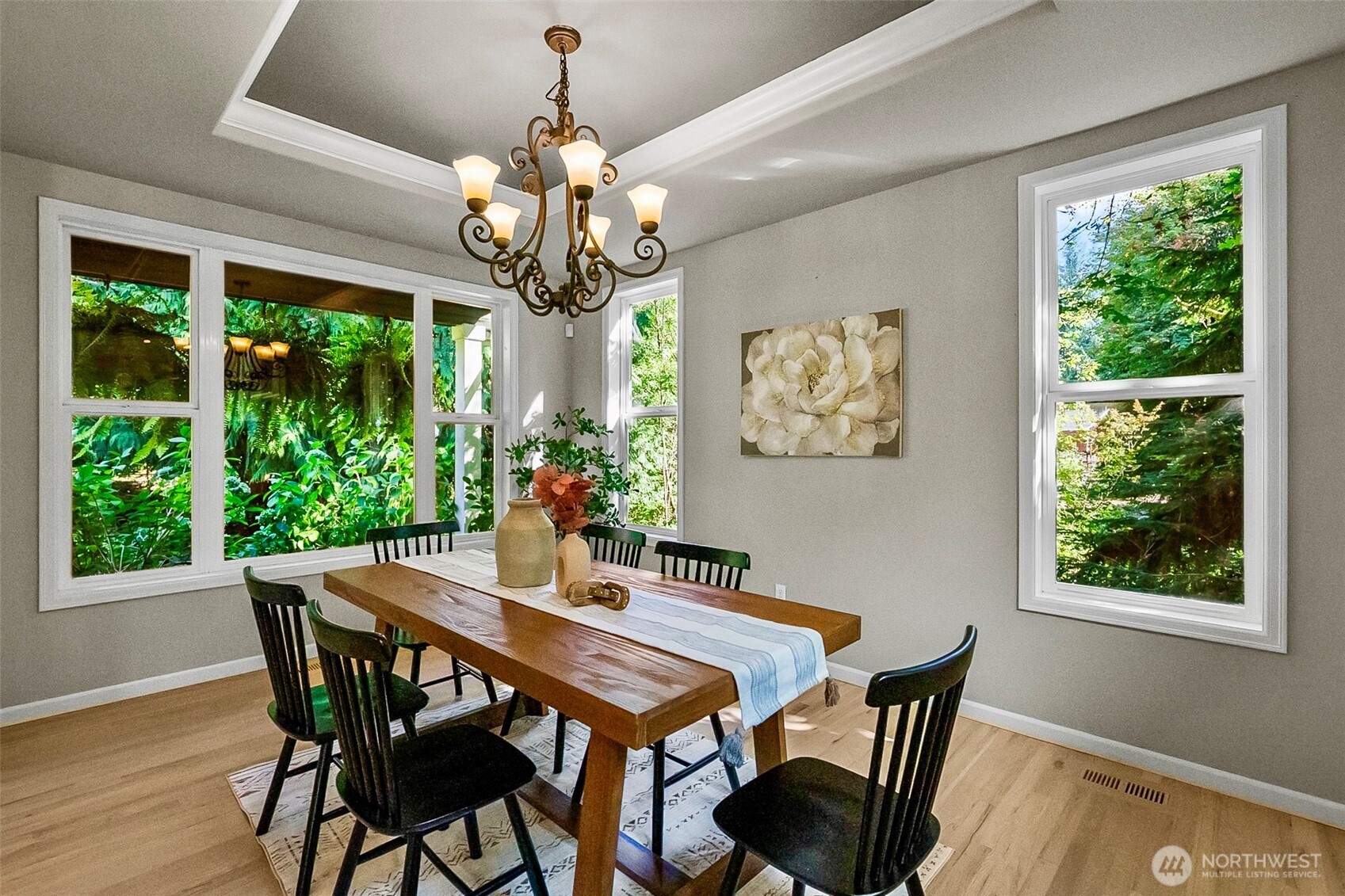 Dining room with a long wood table and large windows overlooking greenery.