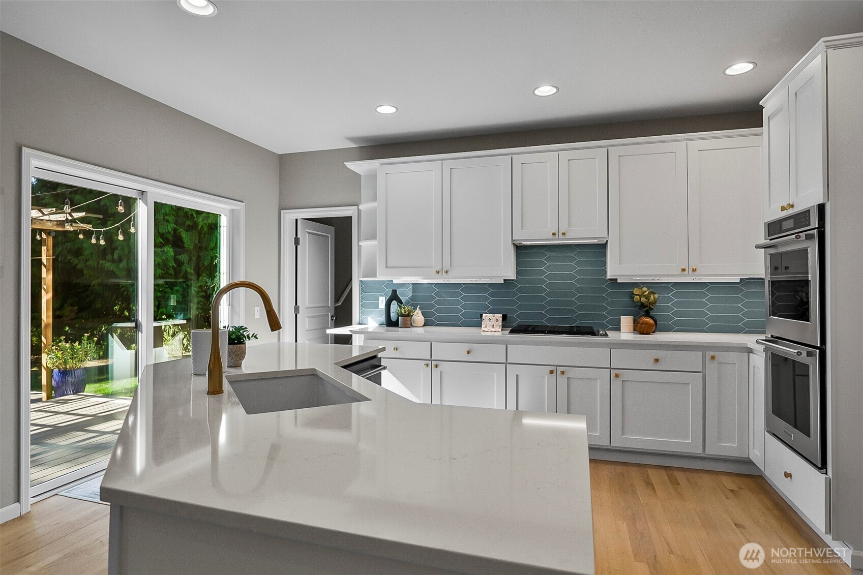 Bright kitchen with a large white island, blue-green tile backsplash, and sliding glass door to a deck.