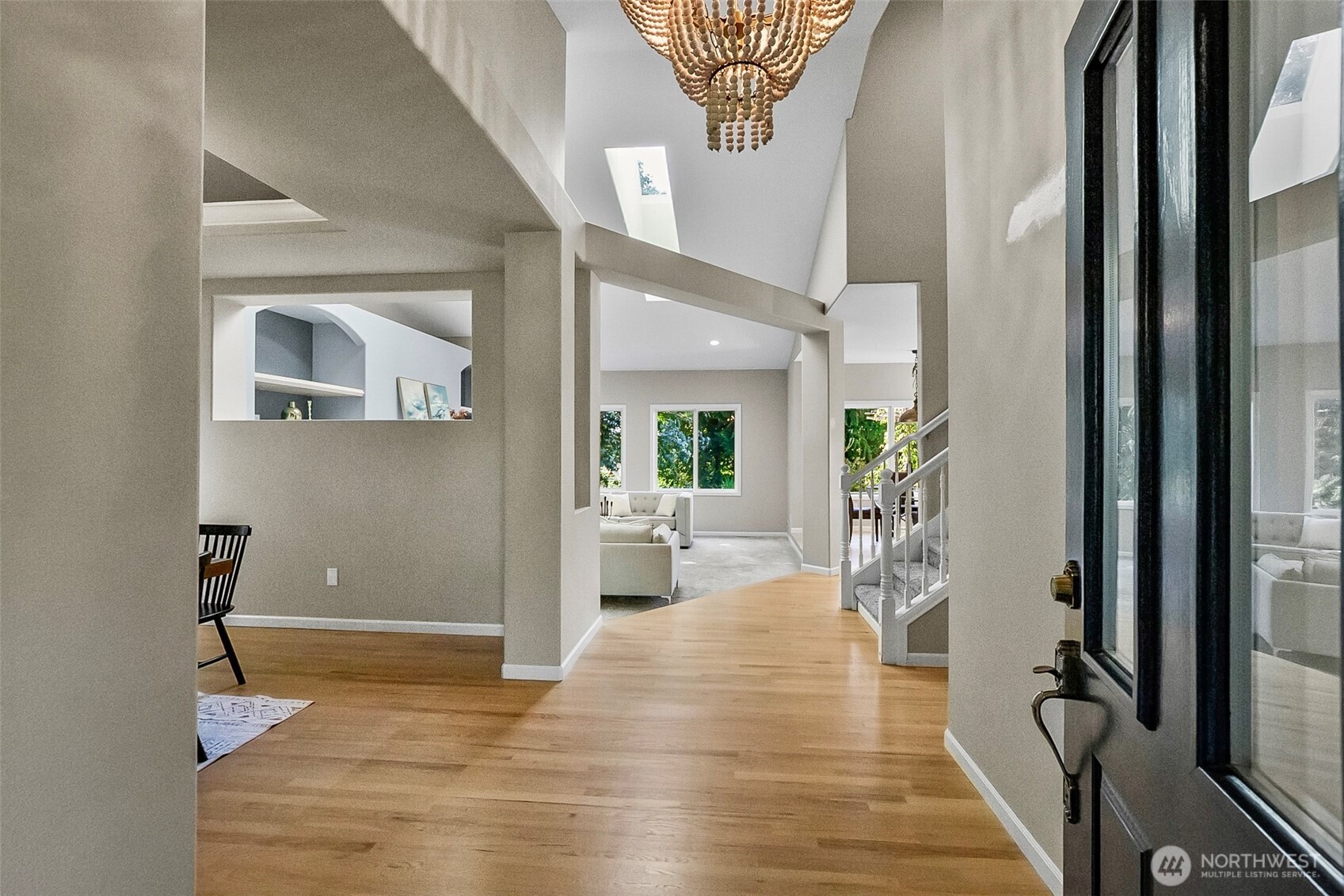 Entryway with hardwood floors, a skylight, beaded chandelier, and staircase opening toward the living room.