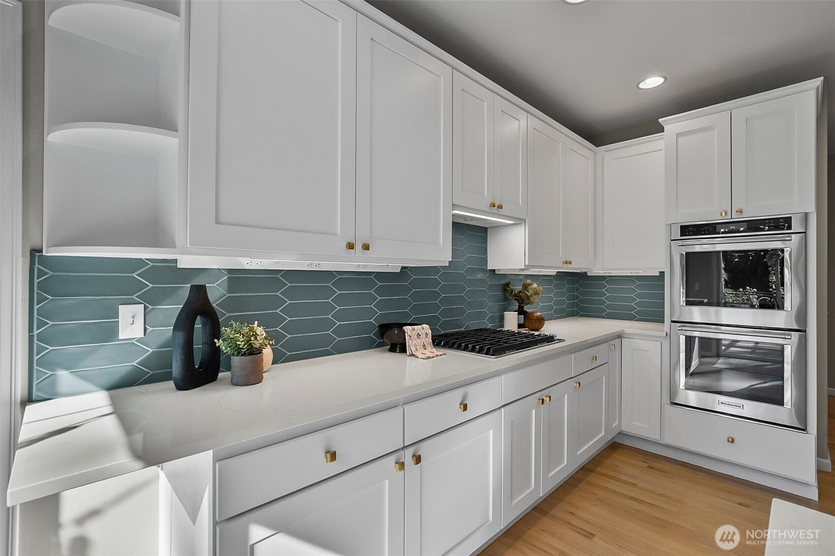 Kitchen with teal geometric backsplash, white cabinetry, gas cooktop, and stacked stainless-steel ovens.