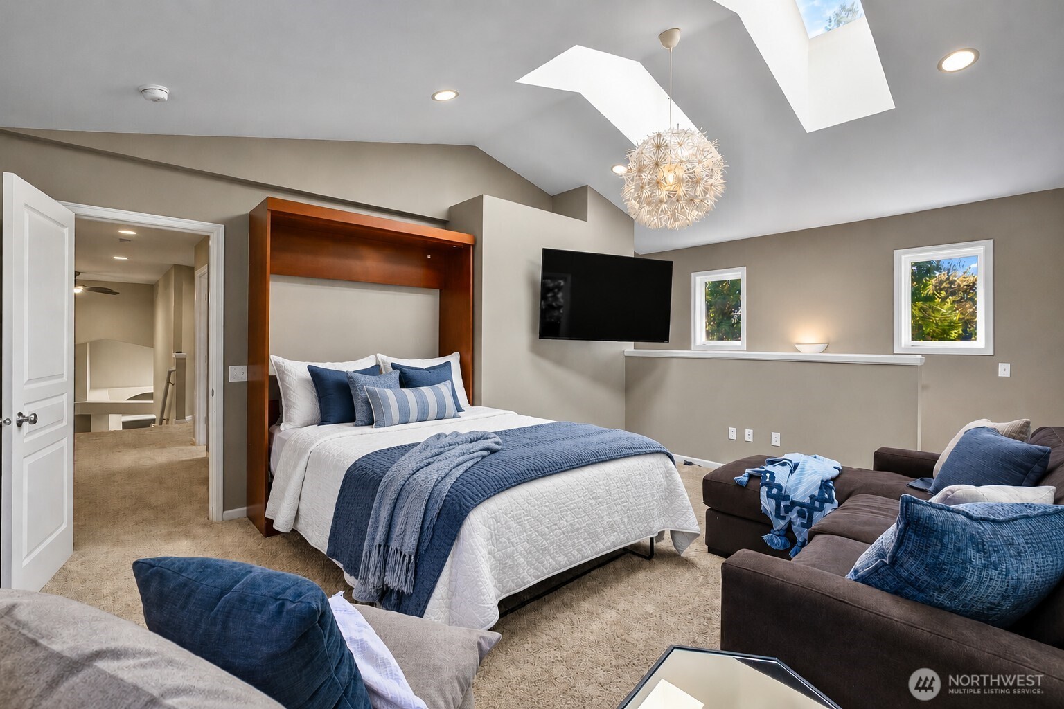 Bedroom with blue bedding, a wood-framed bed, skylights, and an adjoining bathroom doorway.