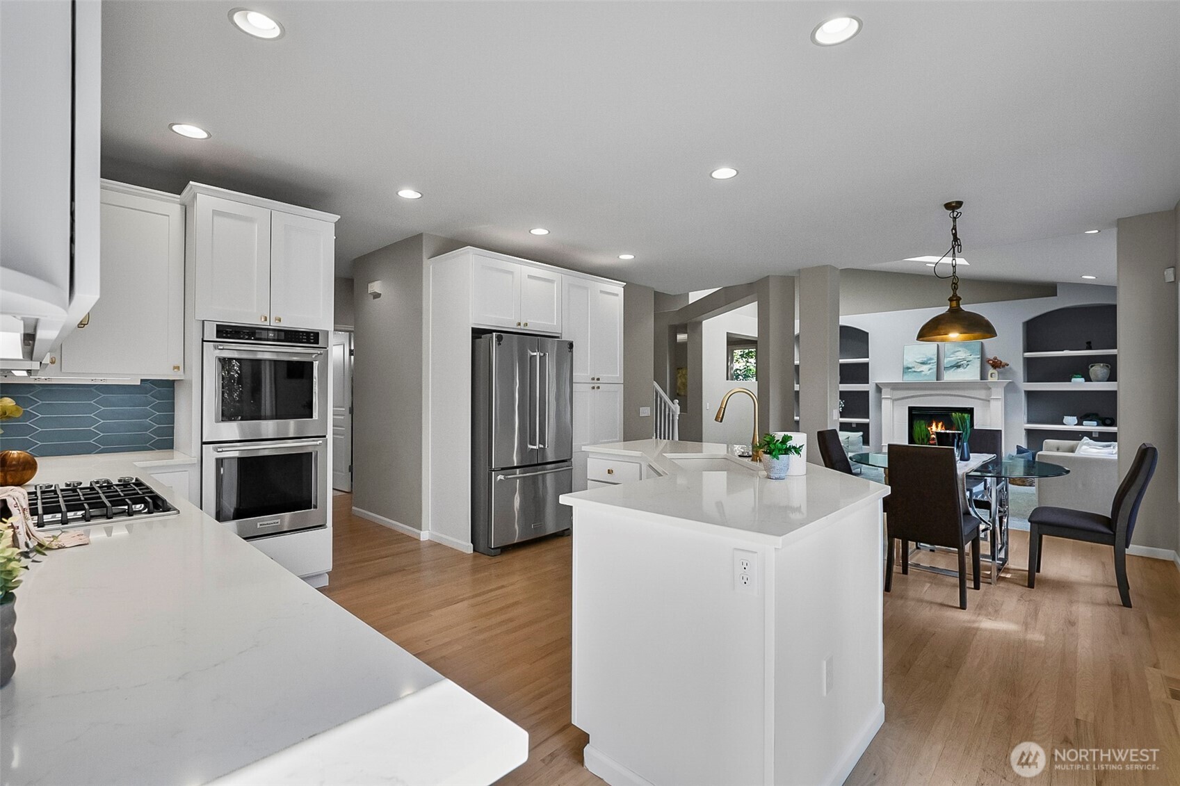 Open kitchen with white cabinets, blue tile backsplash, stainless appliances, and a large island.