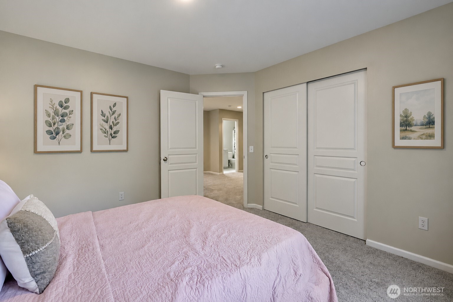 Bedroom with a pink quilted bed, framed botanical prints, and white closet doors.