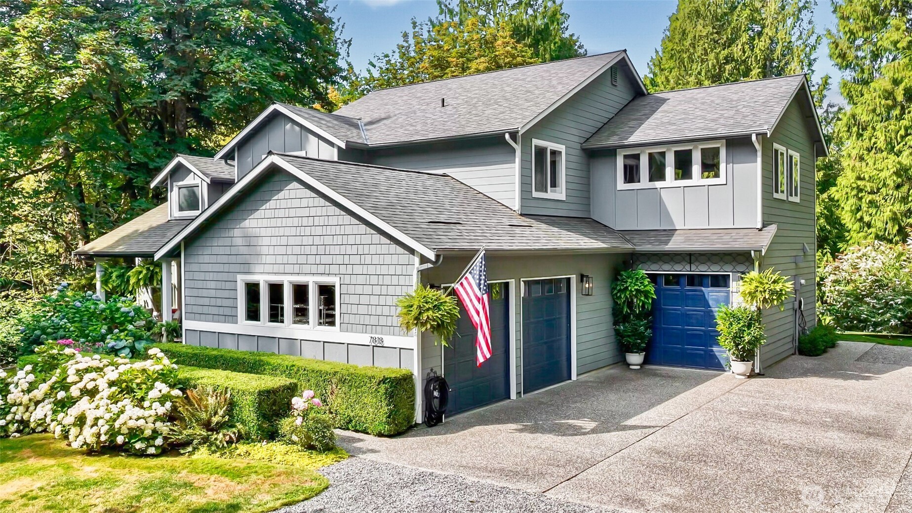 Gray two-story home with blue garage doors, a broad driveway, and flowering landscaping.
