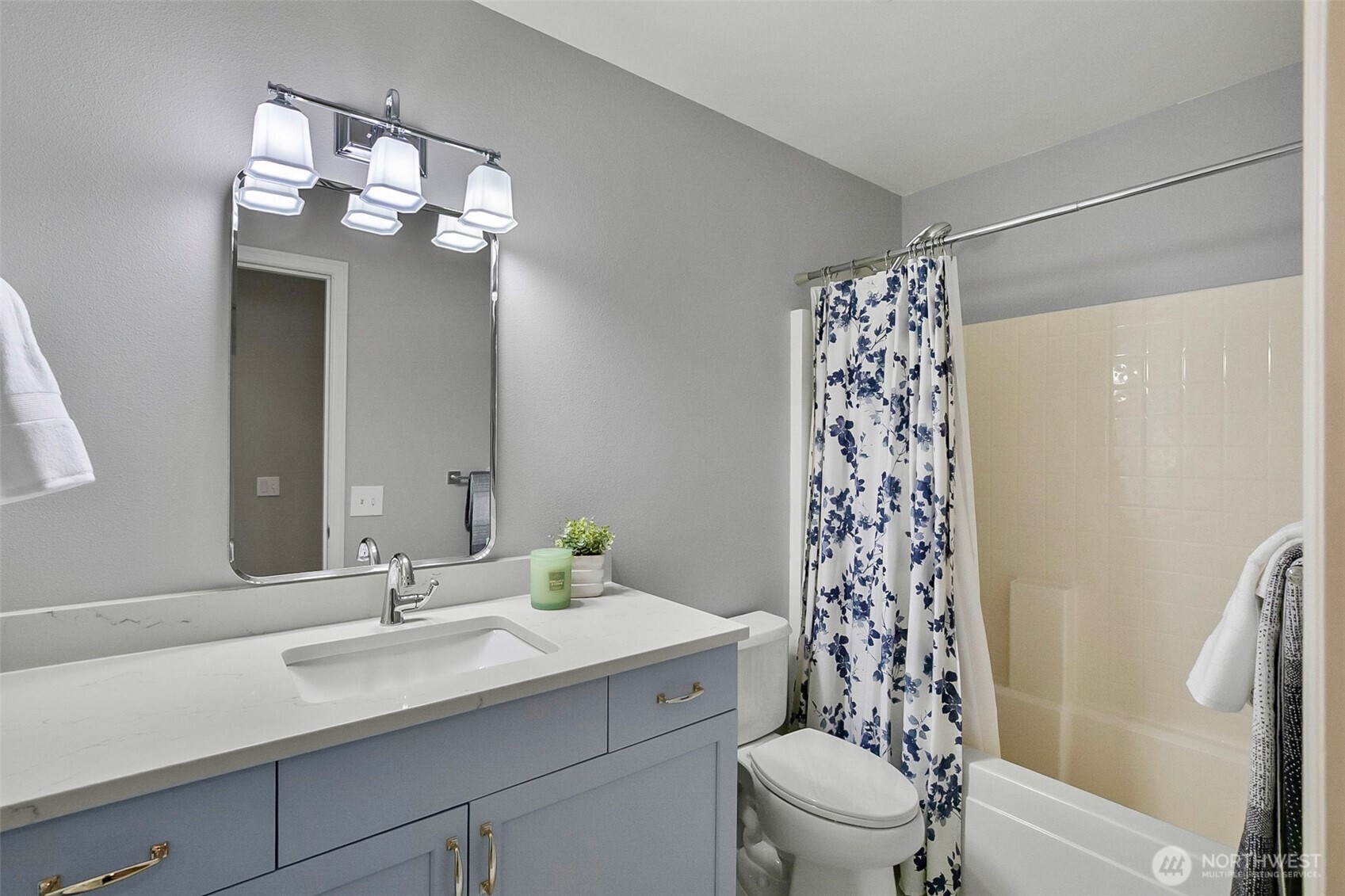 Bathroom with a blue-gray vanity, white countertop, and blue floral shower curtain.