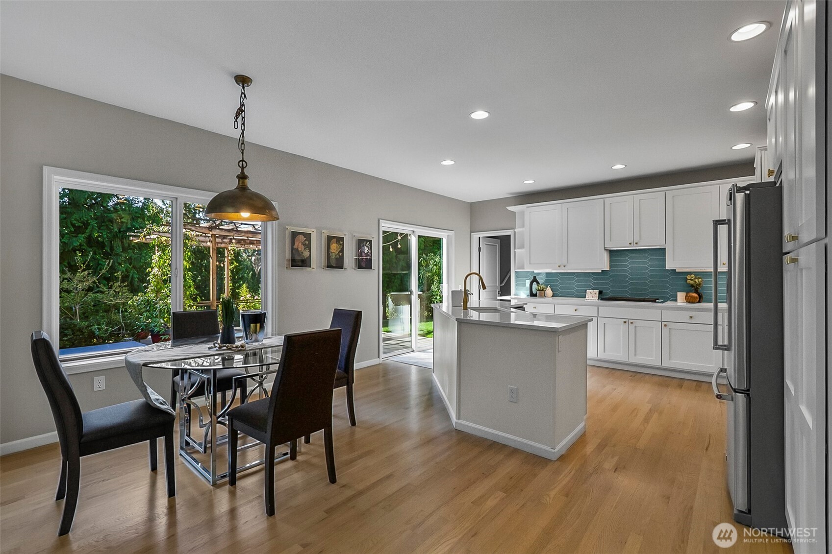Open kitchen and dining area with teal backsplash, central island, and large windows overlooking greenery.