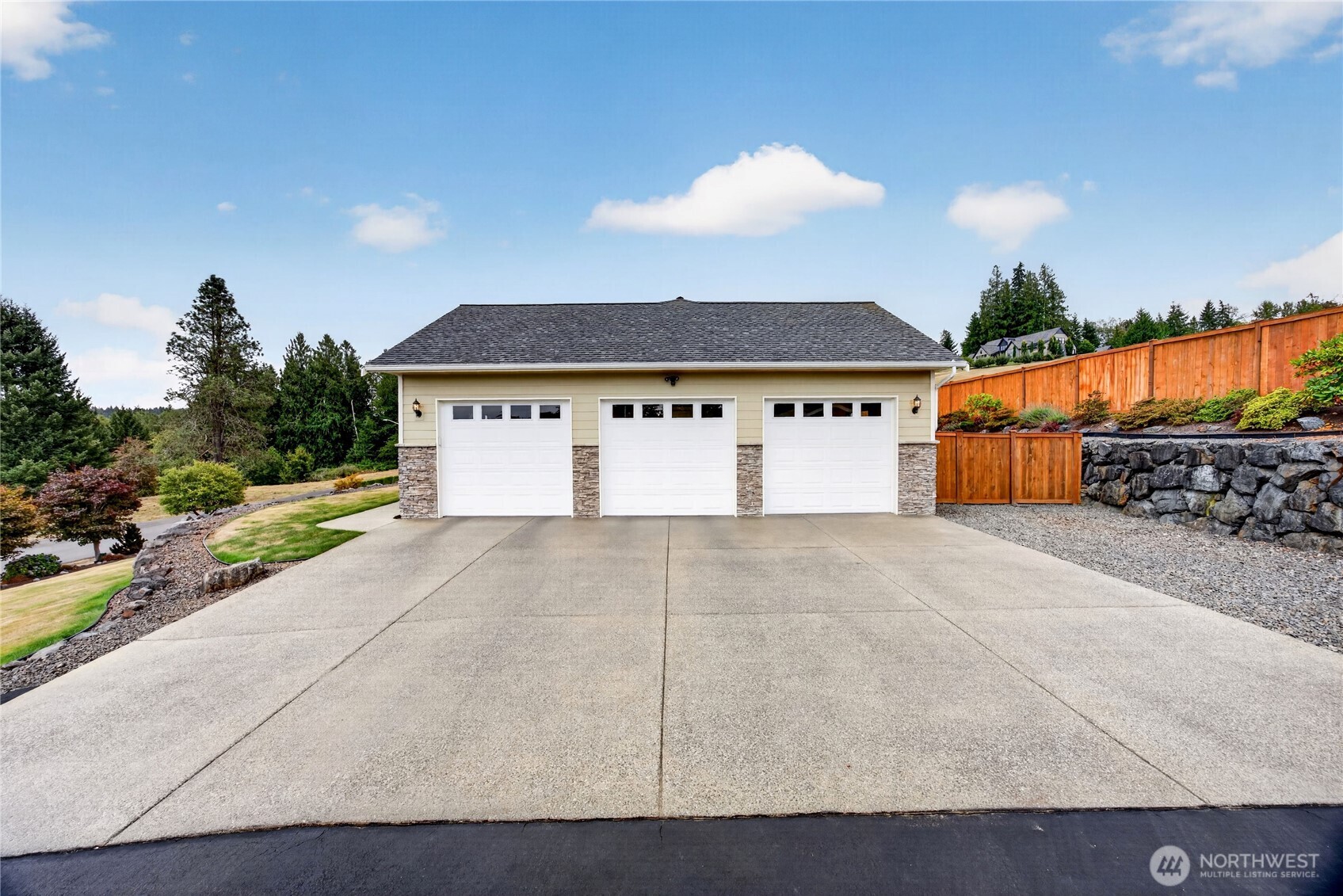 Three-car garage with white doors, stone accents, and a wide concrete driveway.