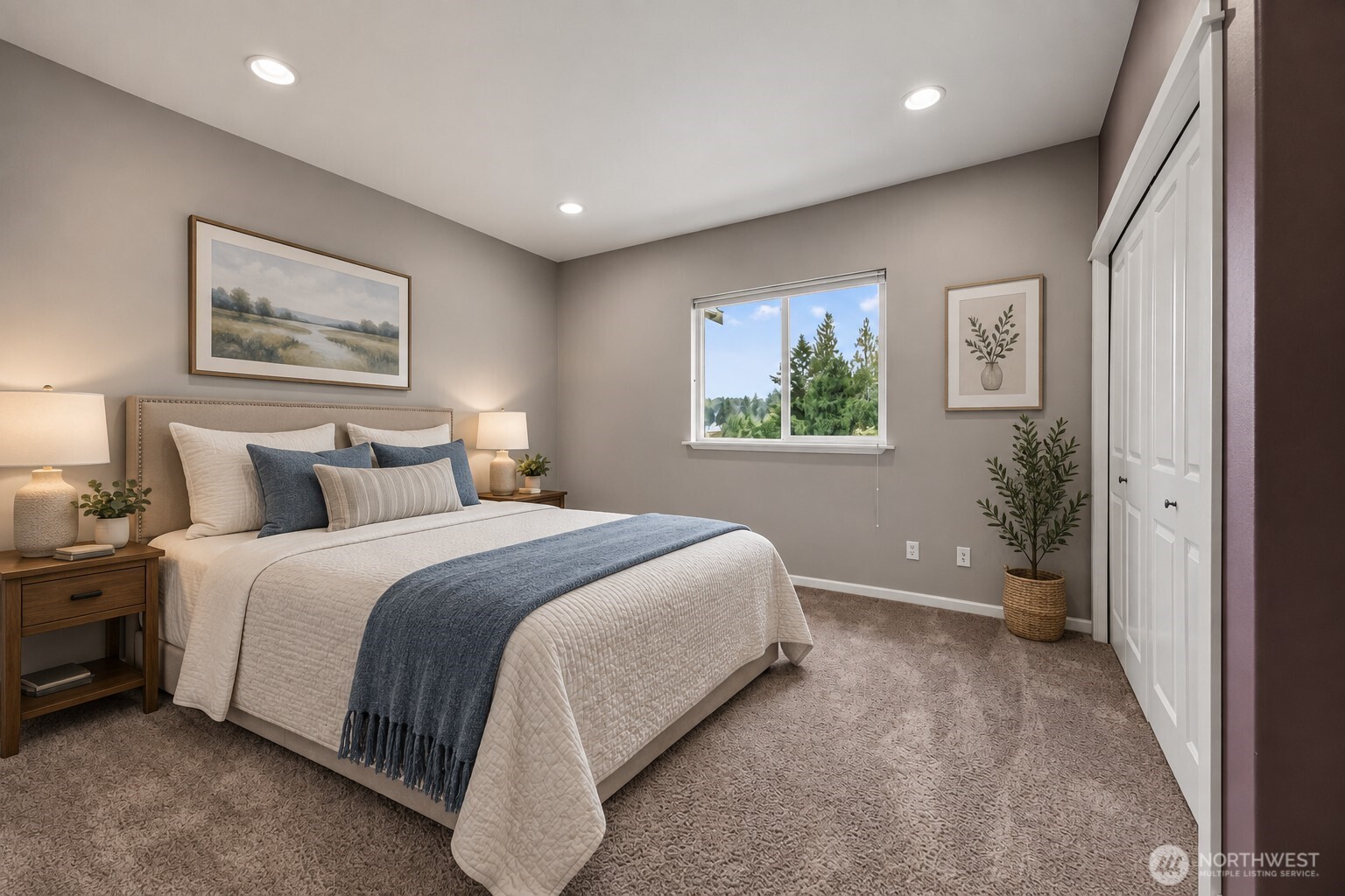 Bedroom with a white bed, blue throw, neutral decor, and a window overlooking trees.