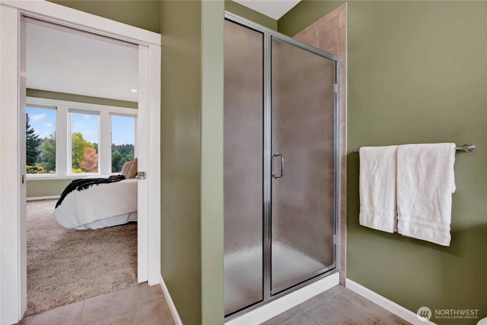 Bathroom with glass-enclosed shower and green walls, opening to a carpeted bedroom.