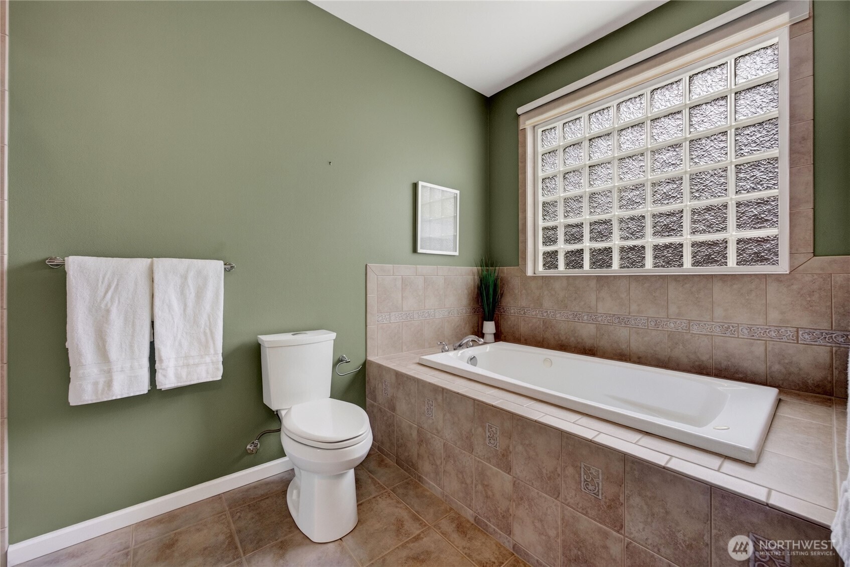 Bathroom with a tiled soaking tub, green walls, and a large textured-glass window.