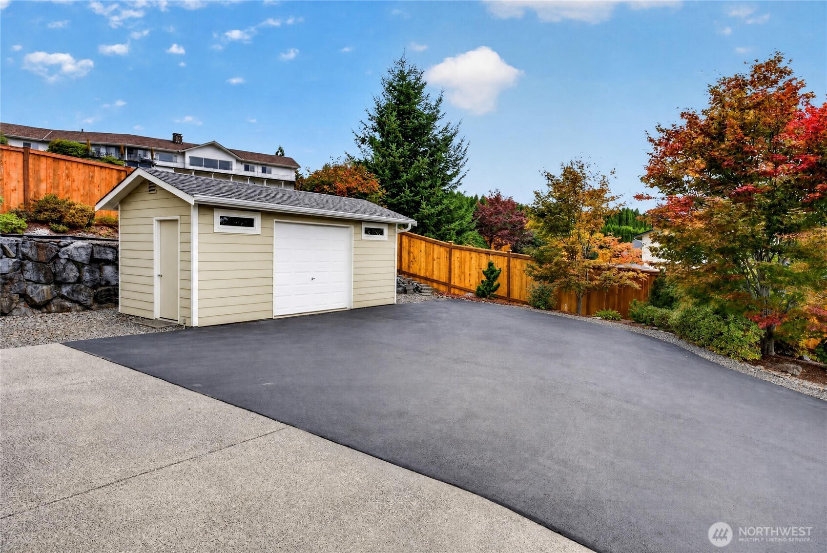 Detached garage beside a broad paved driveway, with autumn trees and wooden fencing.