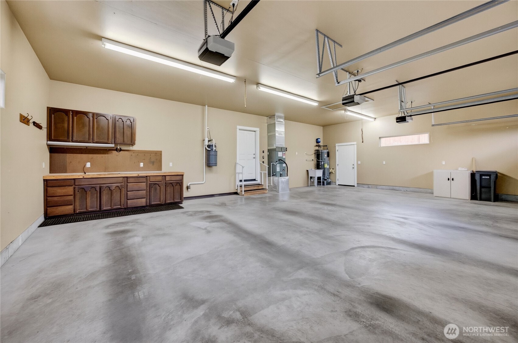 Spacious garage with concrete flooring, overhead door tracks, and a built-in wood workbench.