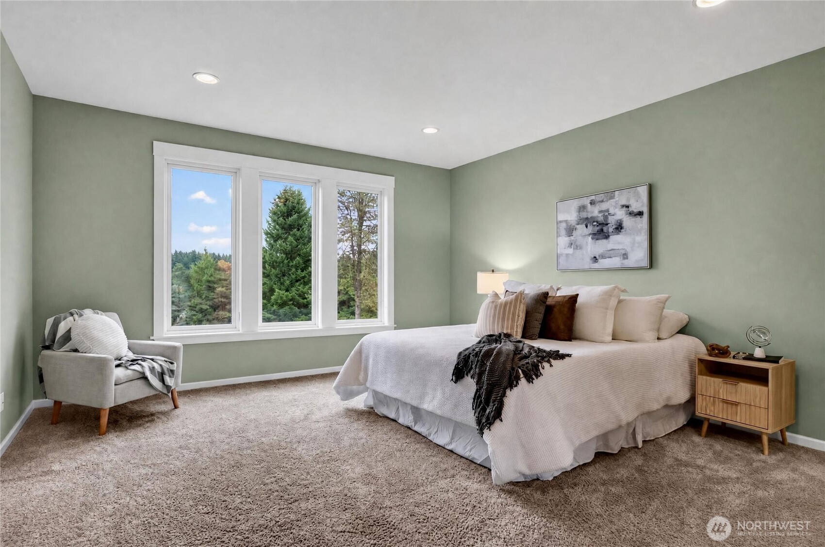 Staged bedroom with sage walls, a large neutral bed, and wide windows overlooking trees.