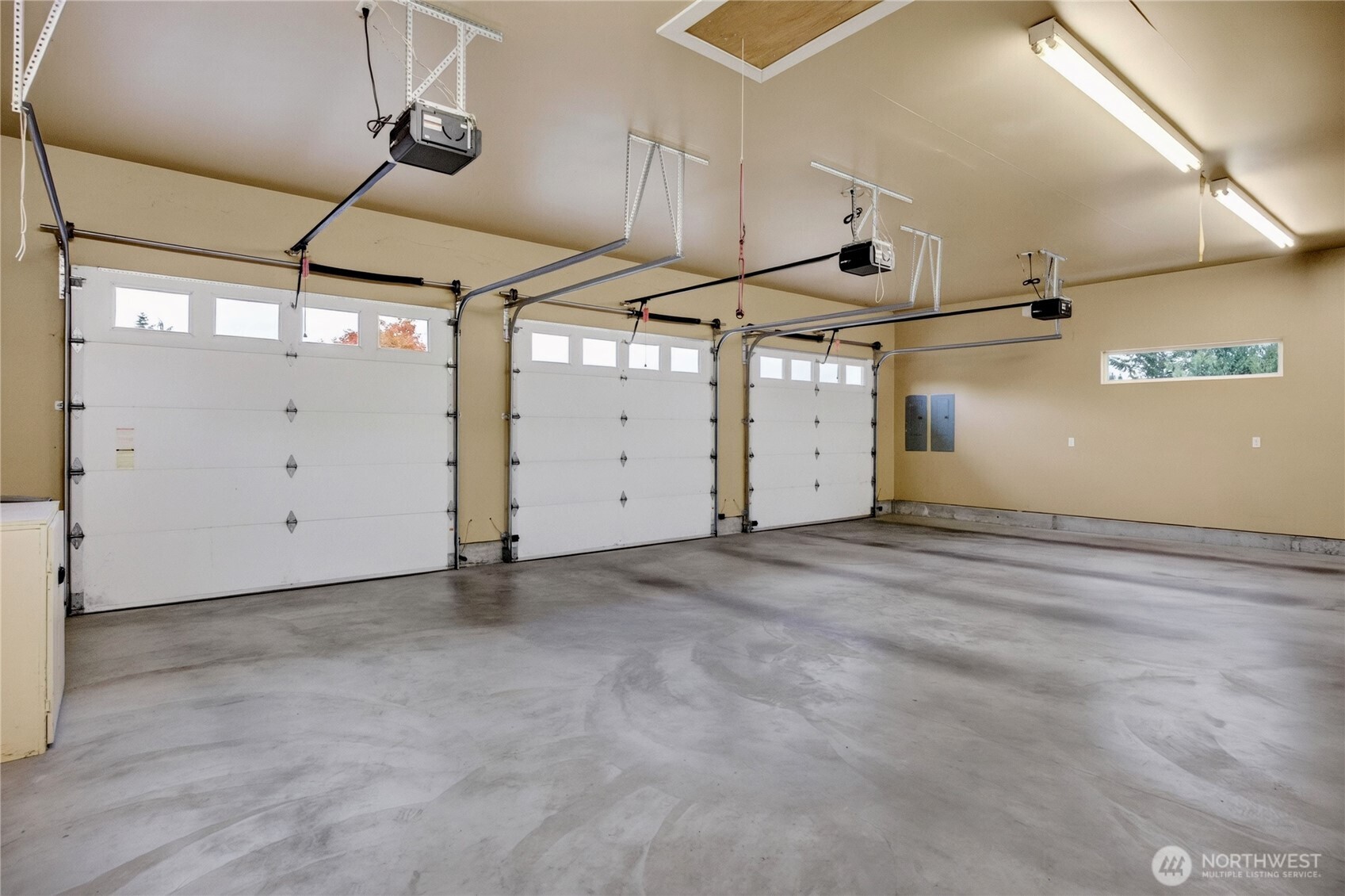 Empty three-car garage with a concrete floor and three white overhead doors.