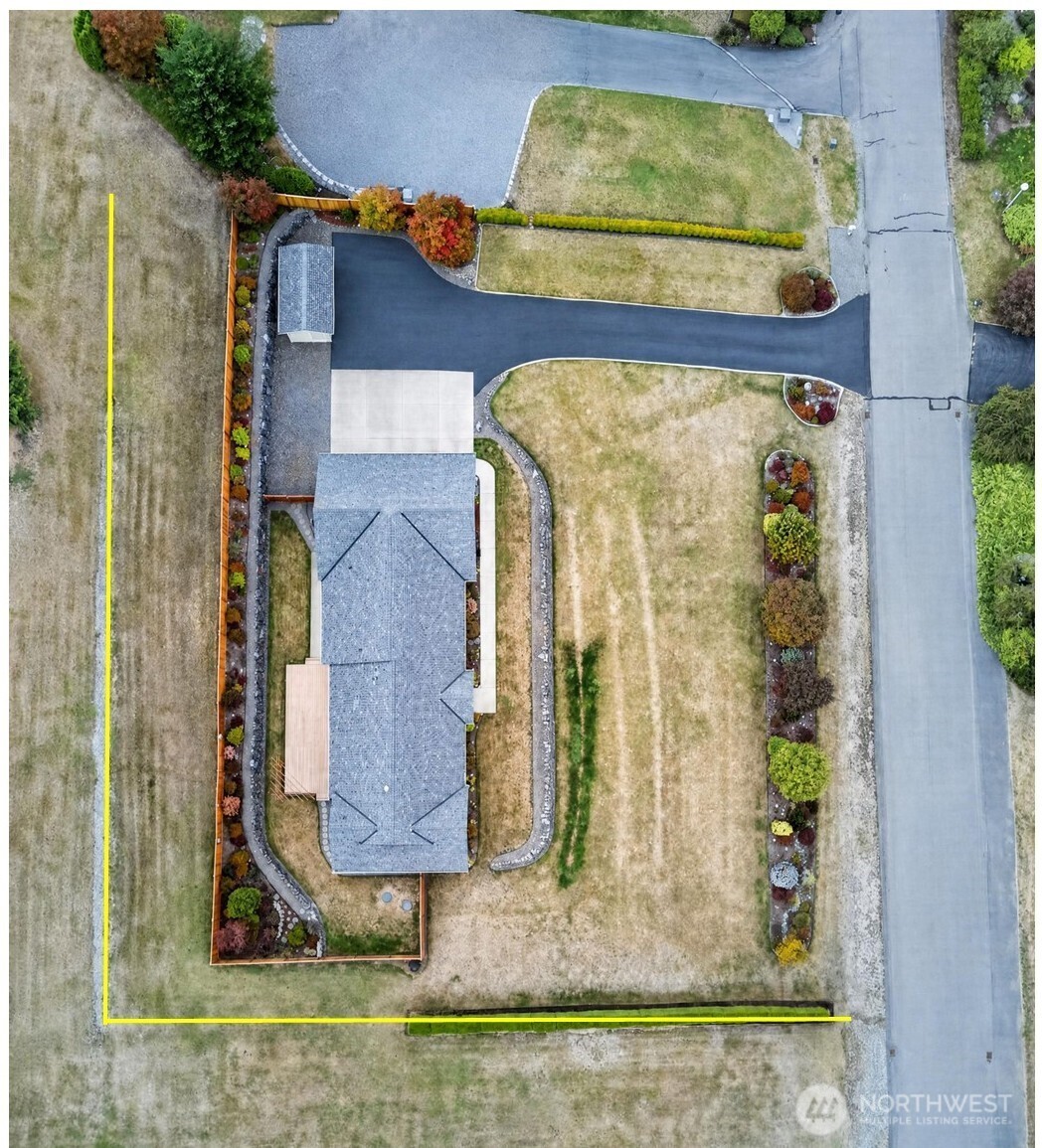 Aerial view of a home with a curved driveway, landscaped yard, and yellow property boundary.