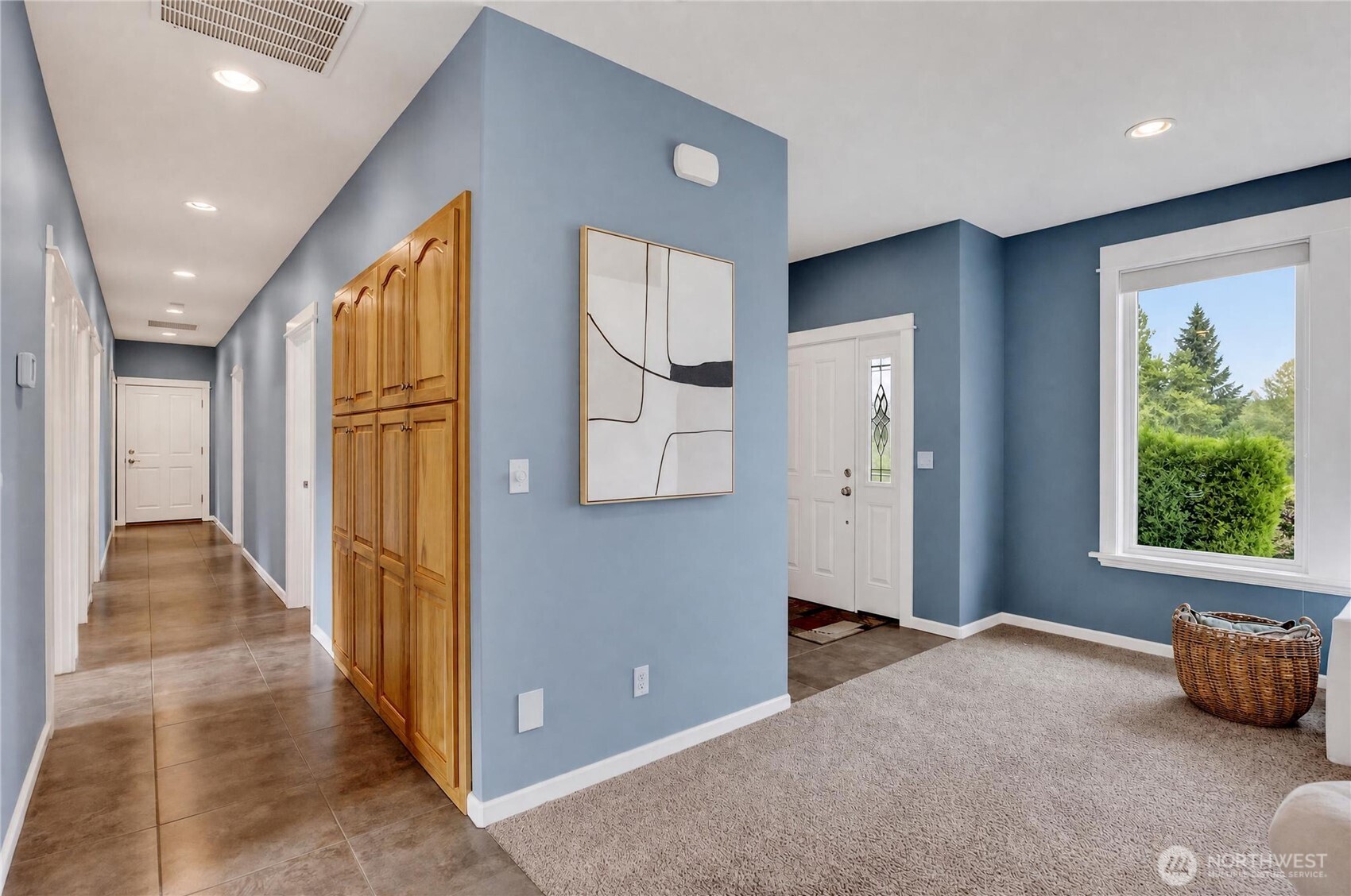 Blue-walled foyer with built-in wood cabinets, tiled hallway, and a large window beside the front door.