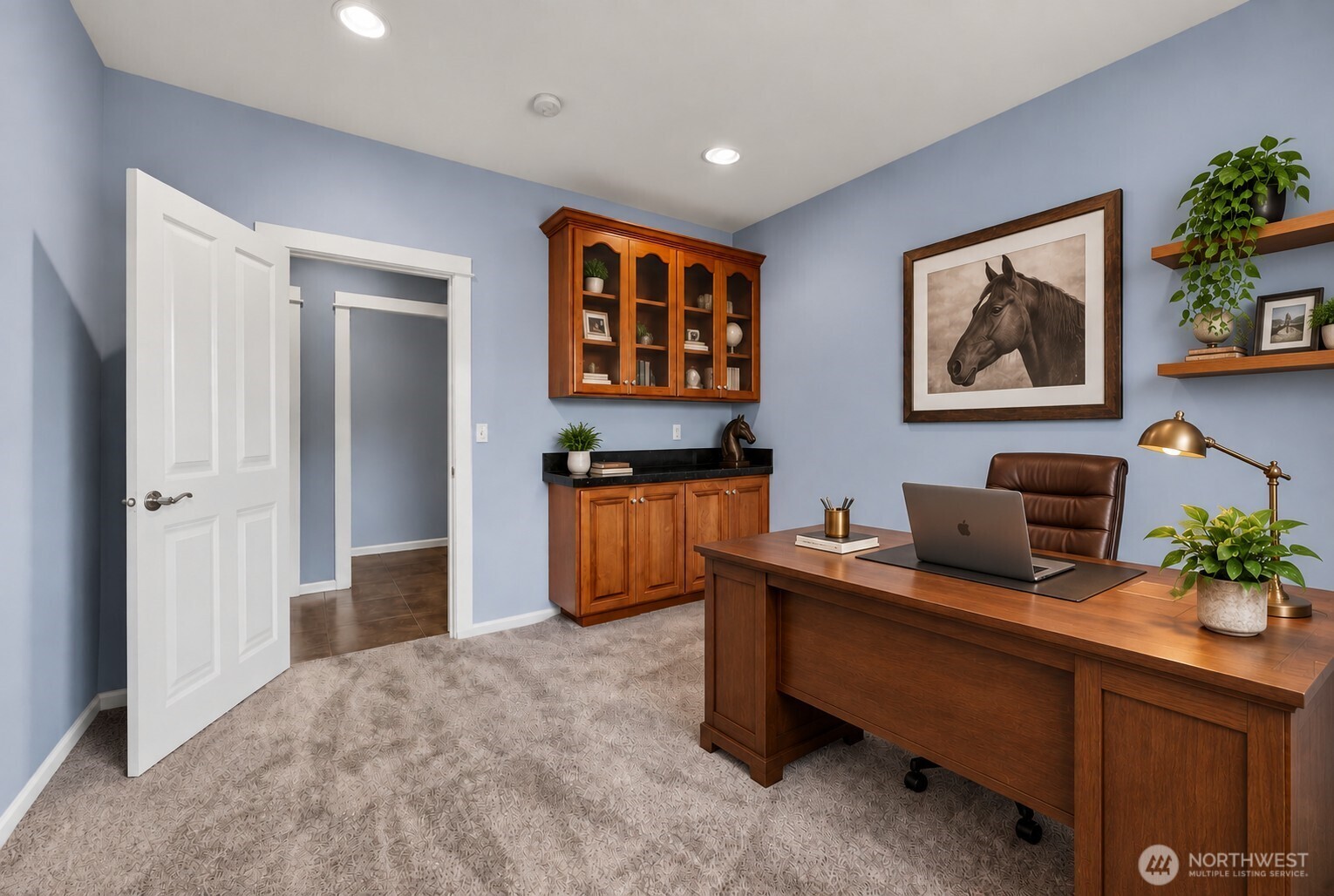 Furnished home office with a large wooden desk, blue walls, and framed horse artwork.