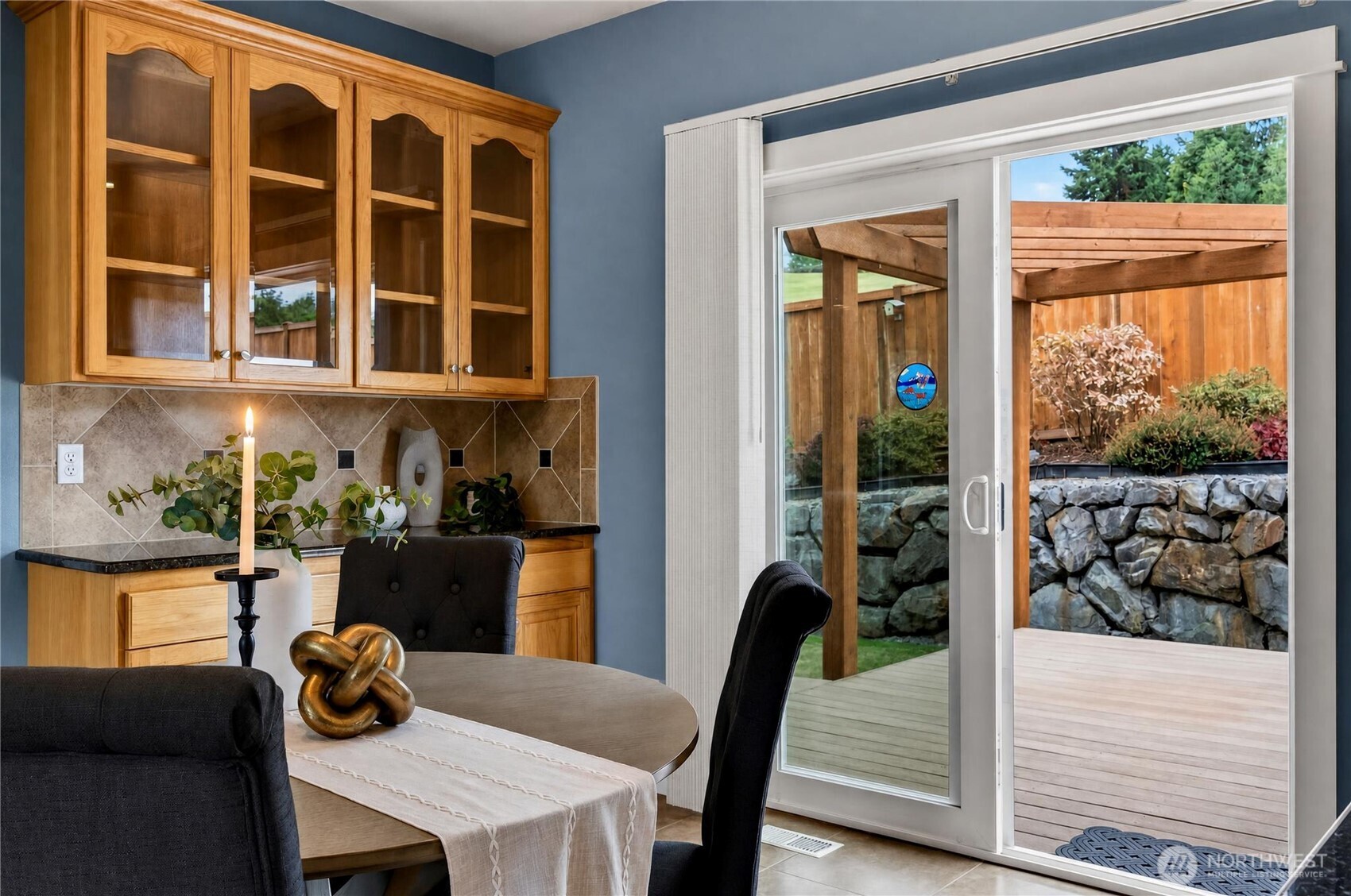 Dining area with glass-front wood cabinets and sliding doors to a deck and landscaped backyard.