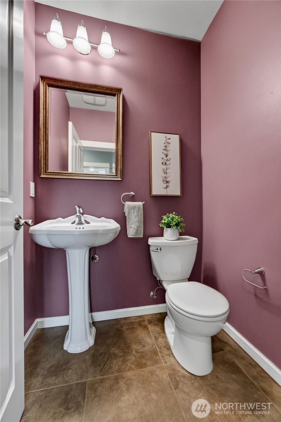 Powder room with mauve walls, a white pedestal sink, and brown tile flooring.