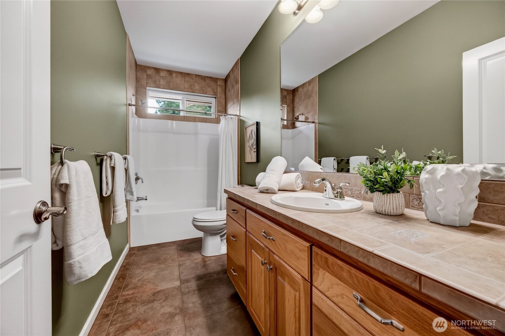 Bathroom with a white tub and shower, toilet, and long wood vanity topped with tan tile.