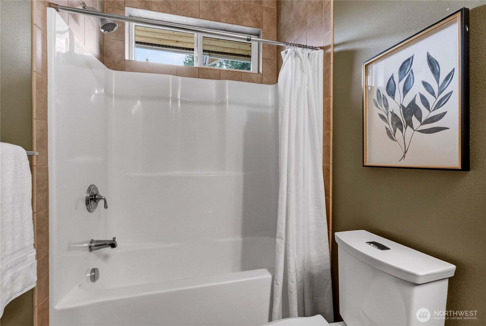 Bathroom with a white tub and shower, high window, and framed botanical print.