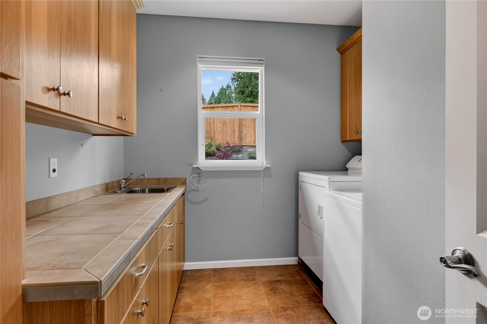Laundry room with washer and dryer, wood cabinetry, and a tiled counter with a sink.