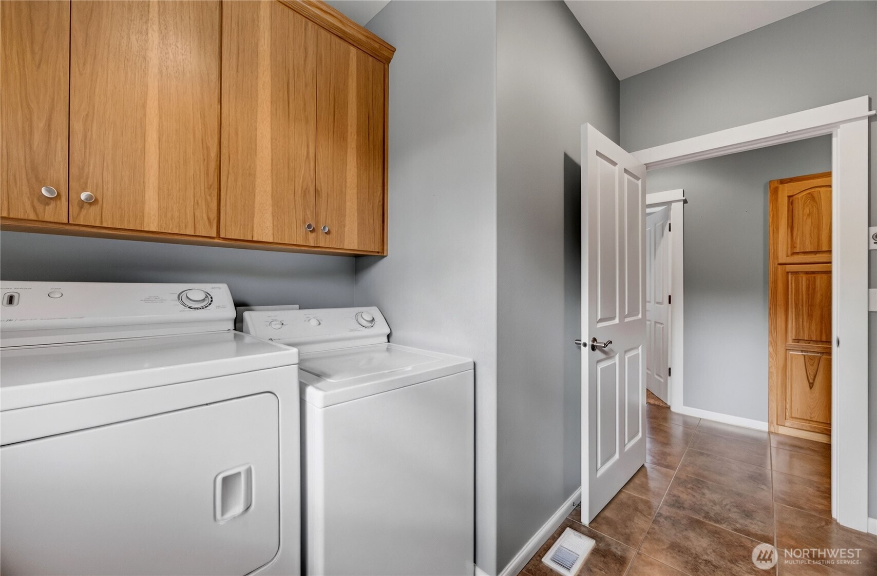 Laundry room with white washer and dryer beneath wood cabinets and an open doorway to the hallway.