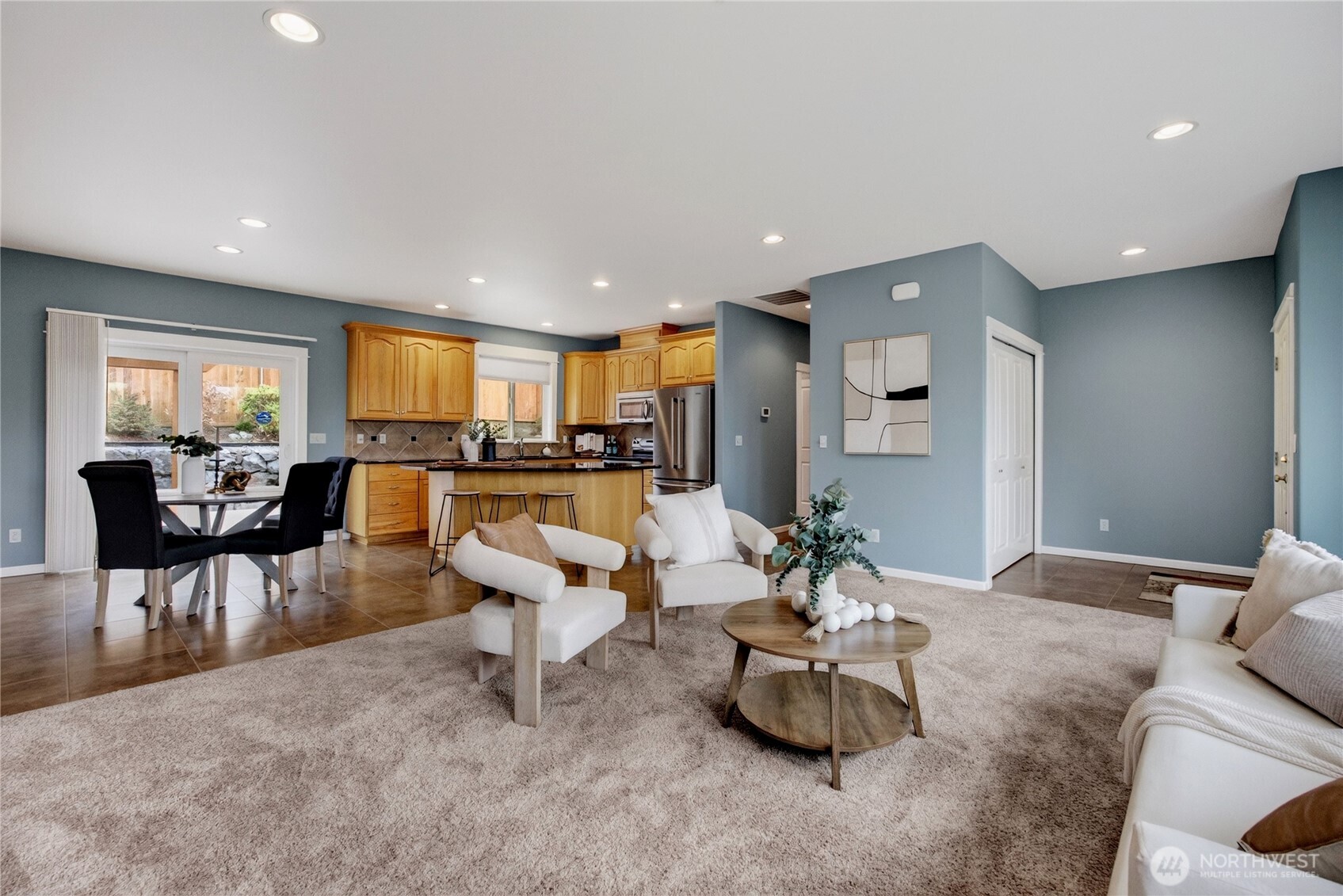Open-plan living room, dining area, and kitchen with honey-colored cabinets and a breakfast bar.