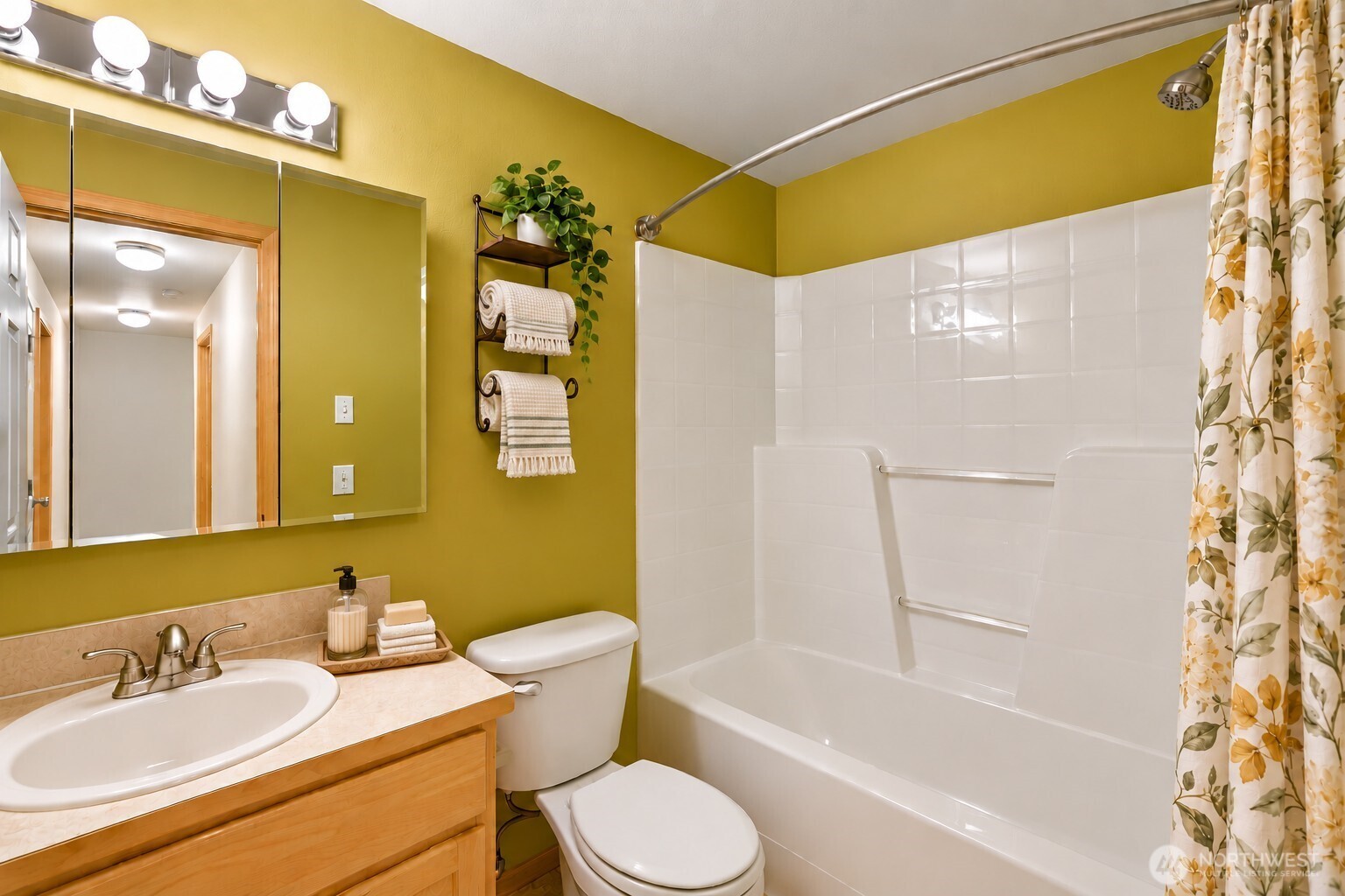 Bathroom with mustard-yellow walls, white tub and shower, toilet, and light wood vanity.