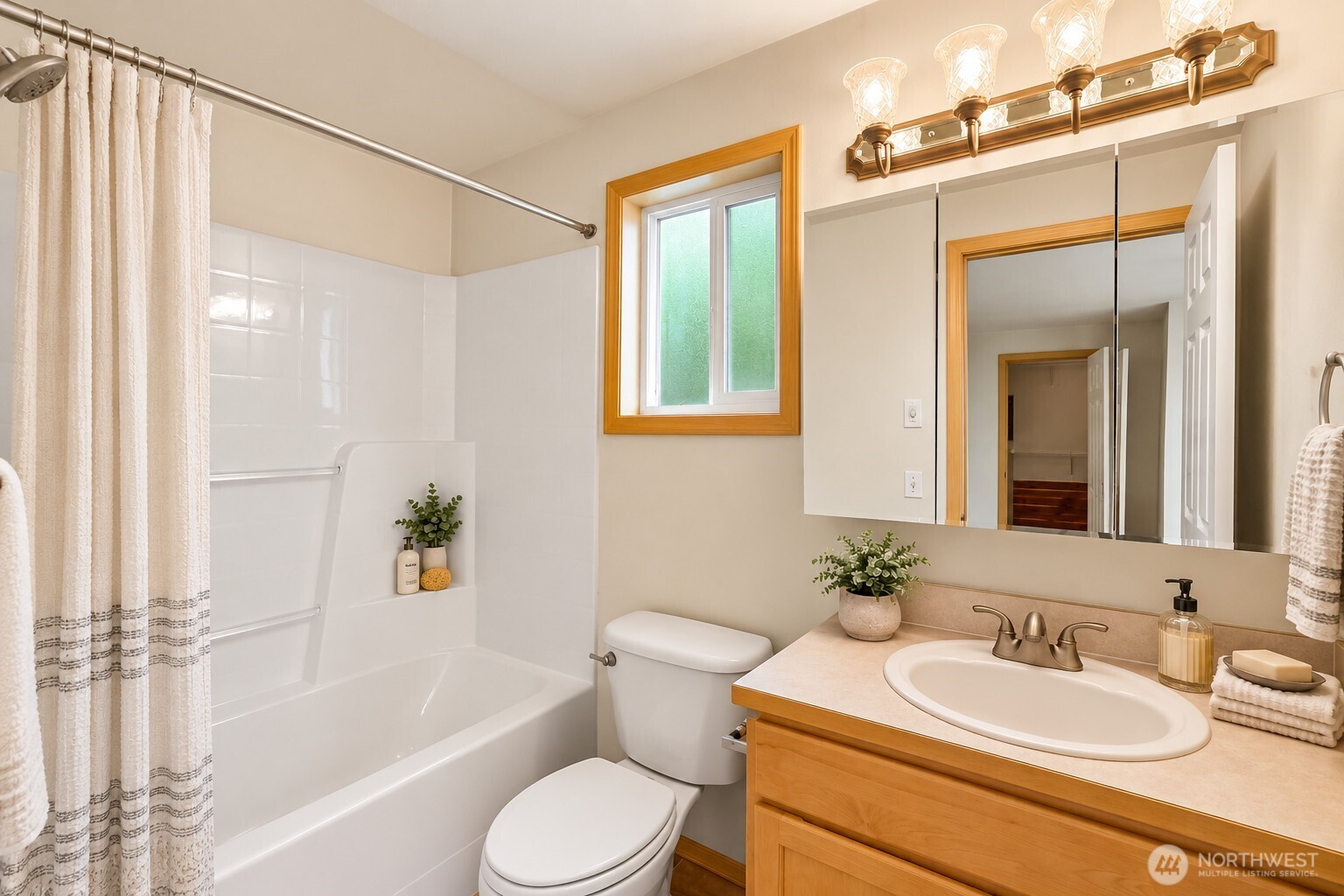 Bathroom with a white tub and shower, wood vanity, oval sink, and mirrored medicine cabinet.