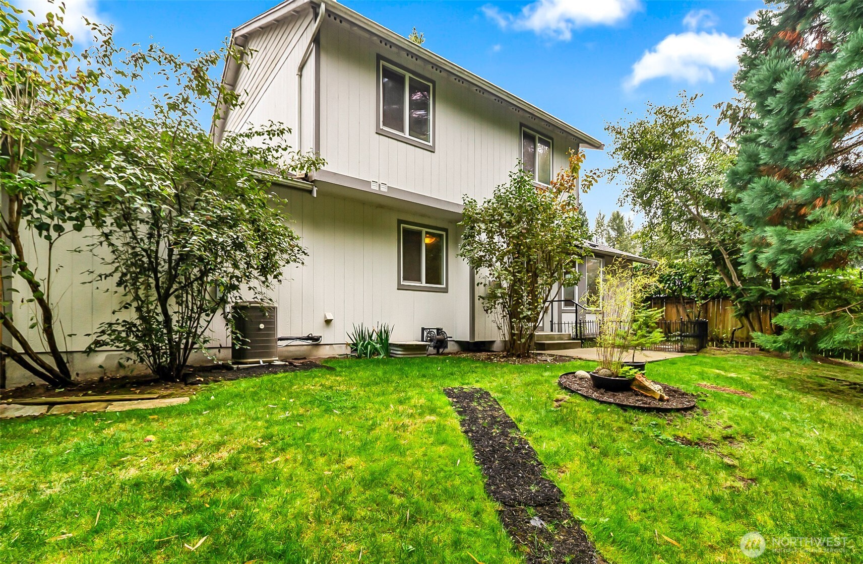 Two-story home behind a green lawn, with mature trees and a fenced backyard.
