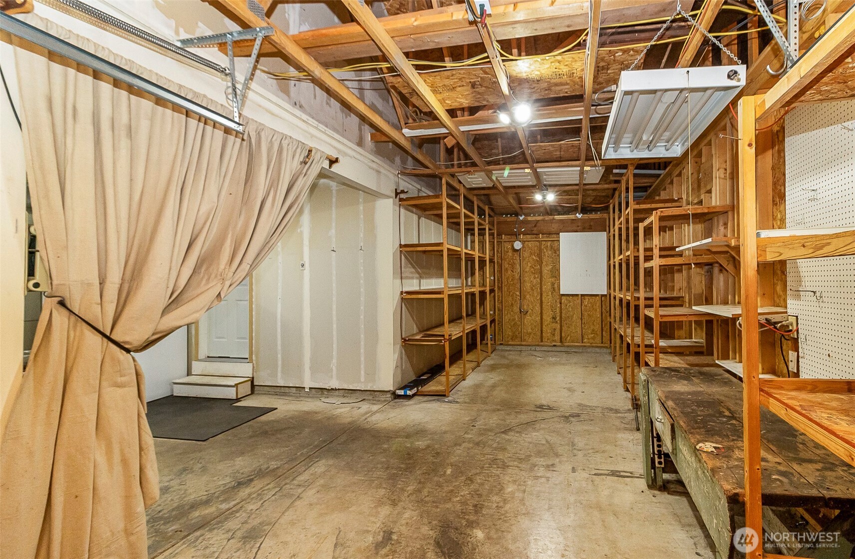 Garage workshop with exposed rafters, concrete floor, and extensive wooden shelving.