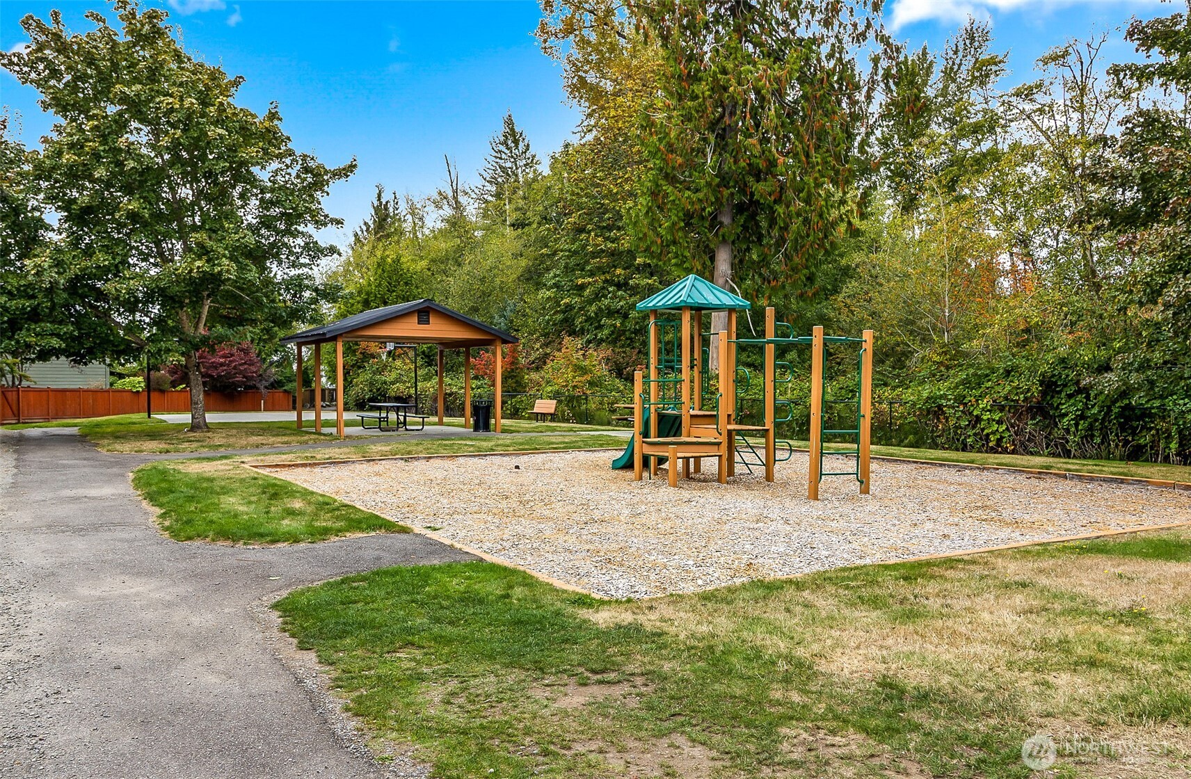 Outdoor playground with a climbing structure, covered picnic area, and mature trees.