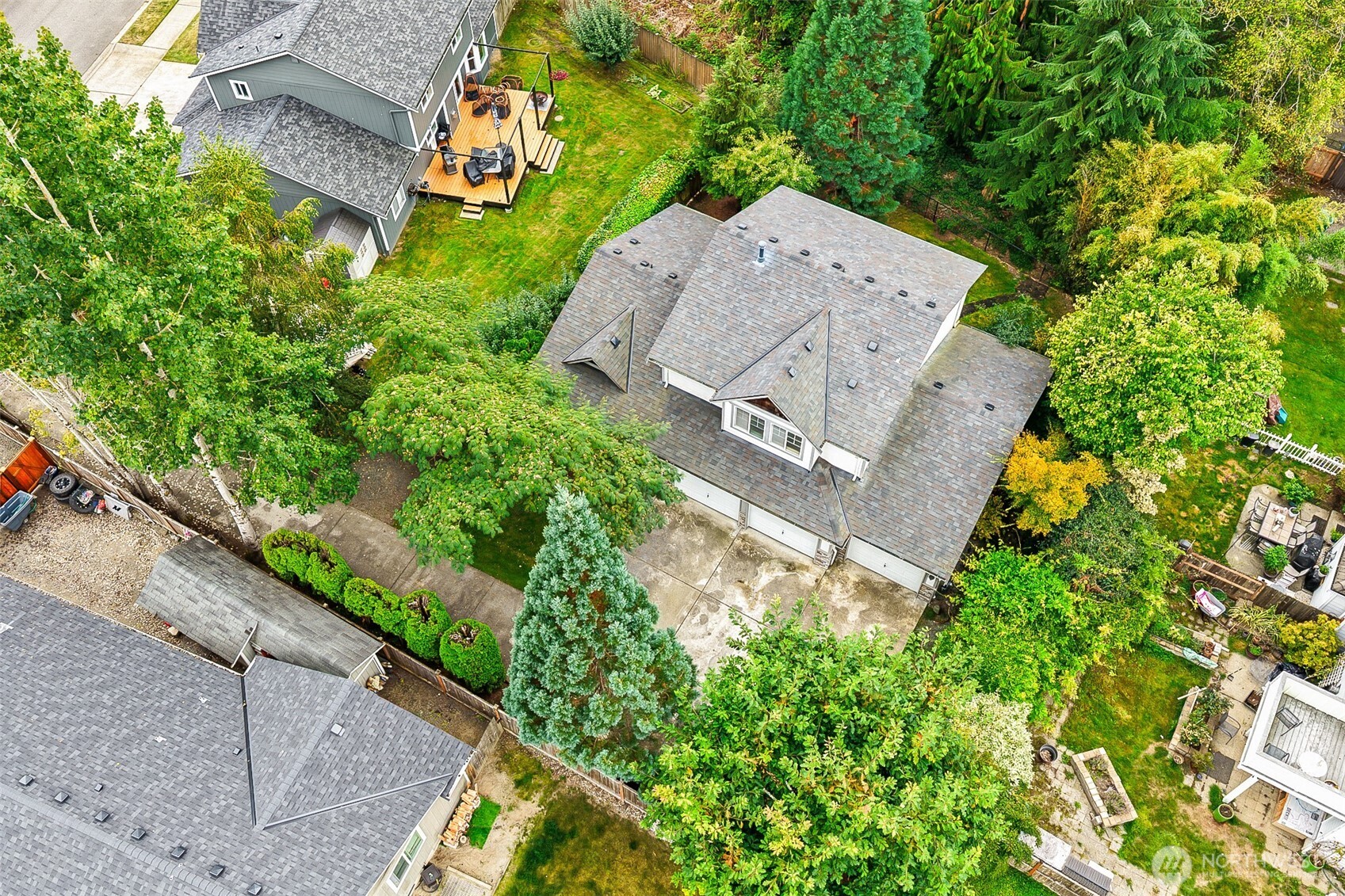Aerial view of a gray-roofed home surrounded by mature trees, landscaped yards, and an outdoor deck.