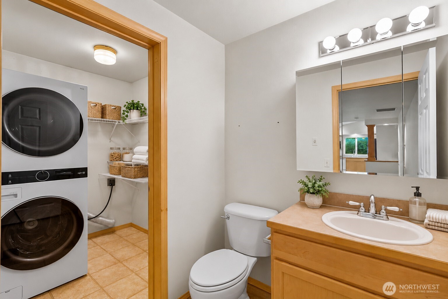 Bathroom with a wood vanity and mirrored cabinet beside a laundry nook with a stacked washer and dryer.