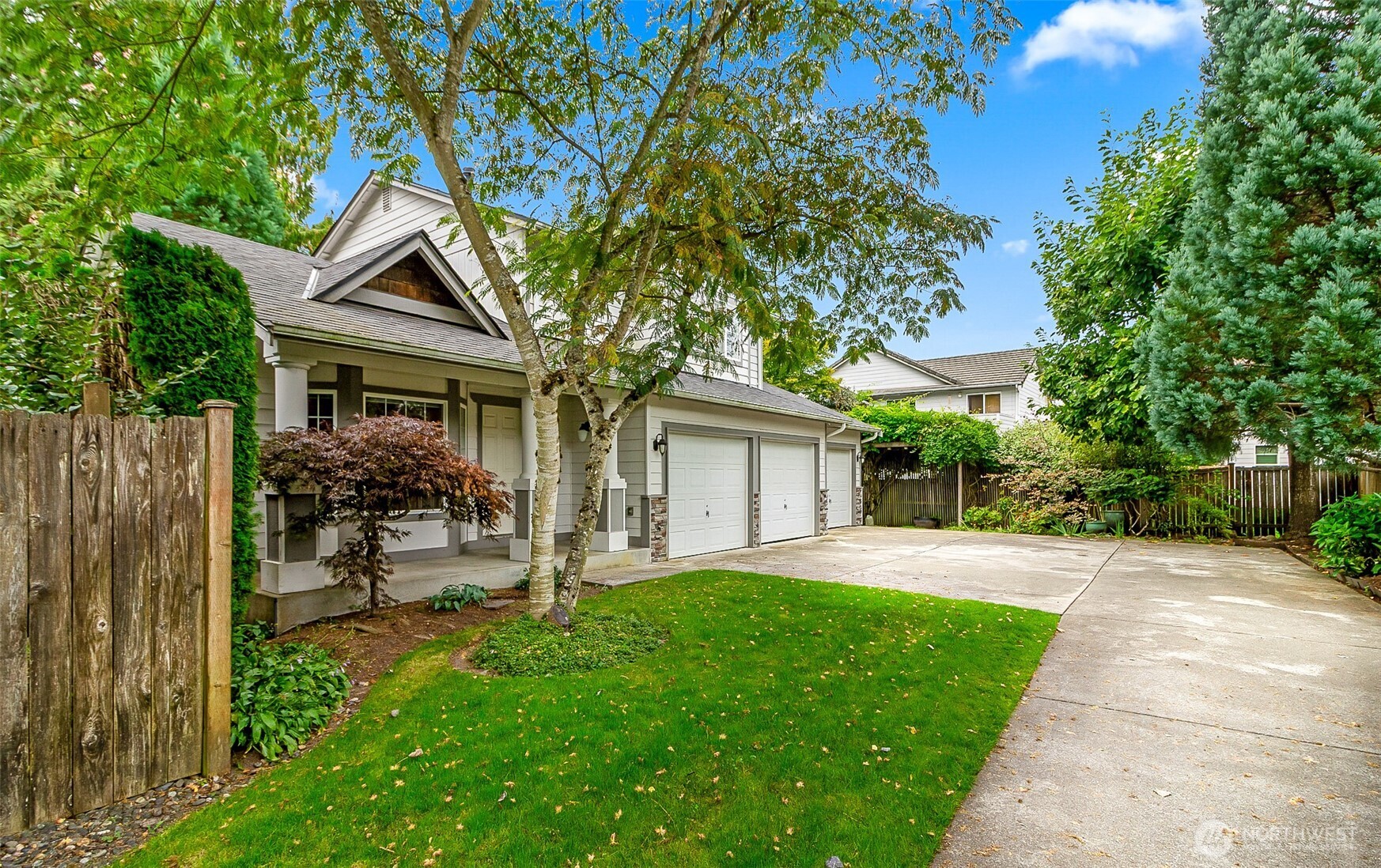 Gray two-story house with a covered porch, two-car garage, mature trees, and a wide driveway.