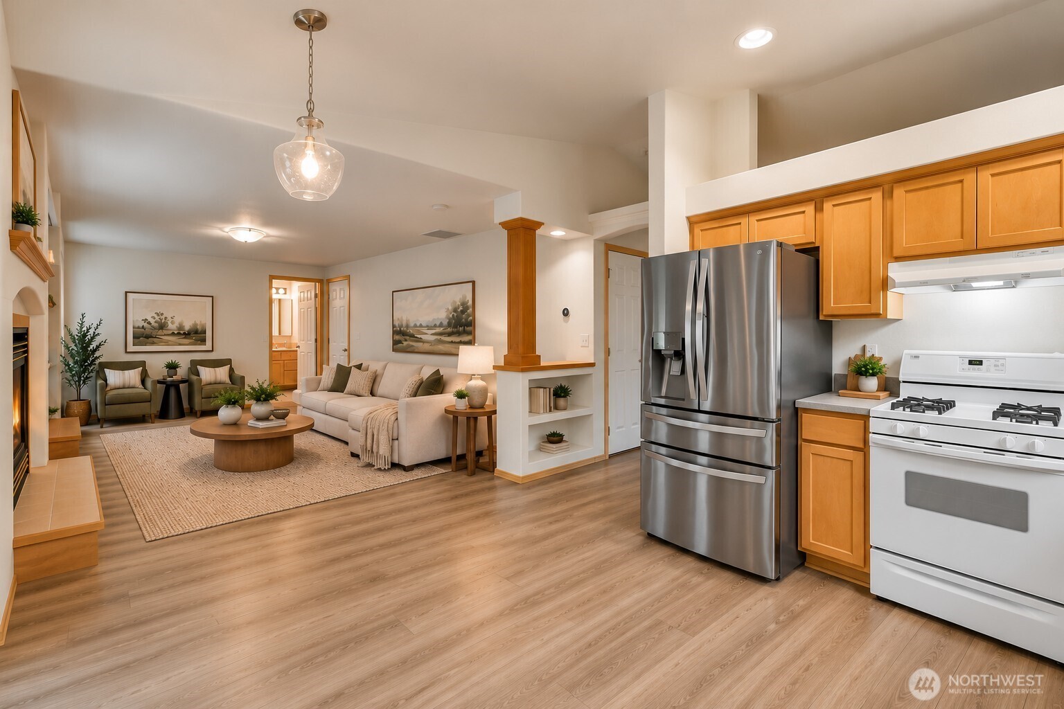 Open-plan kitchen and living room with wood cabinets, stainless appliances, and a furnished seating area.